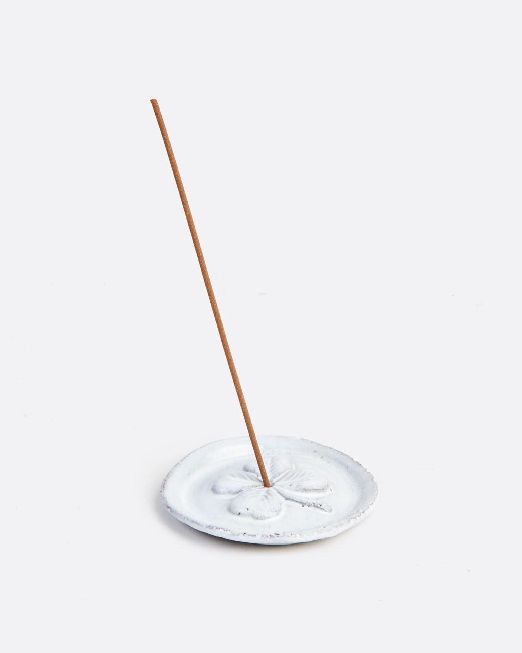 A circular white incense holder with a shamrock on it with an incense stick in it. Shown from the side.