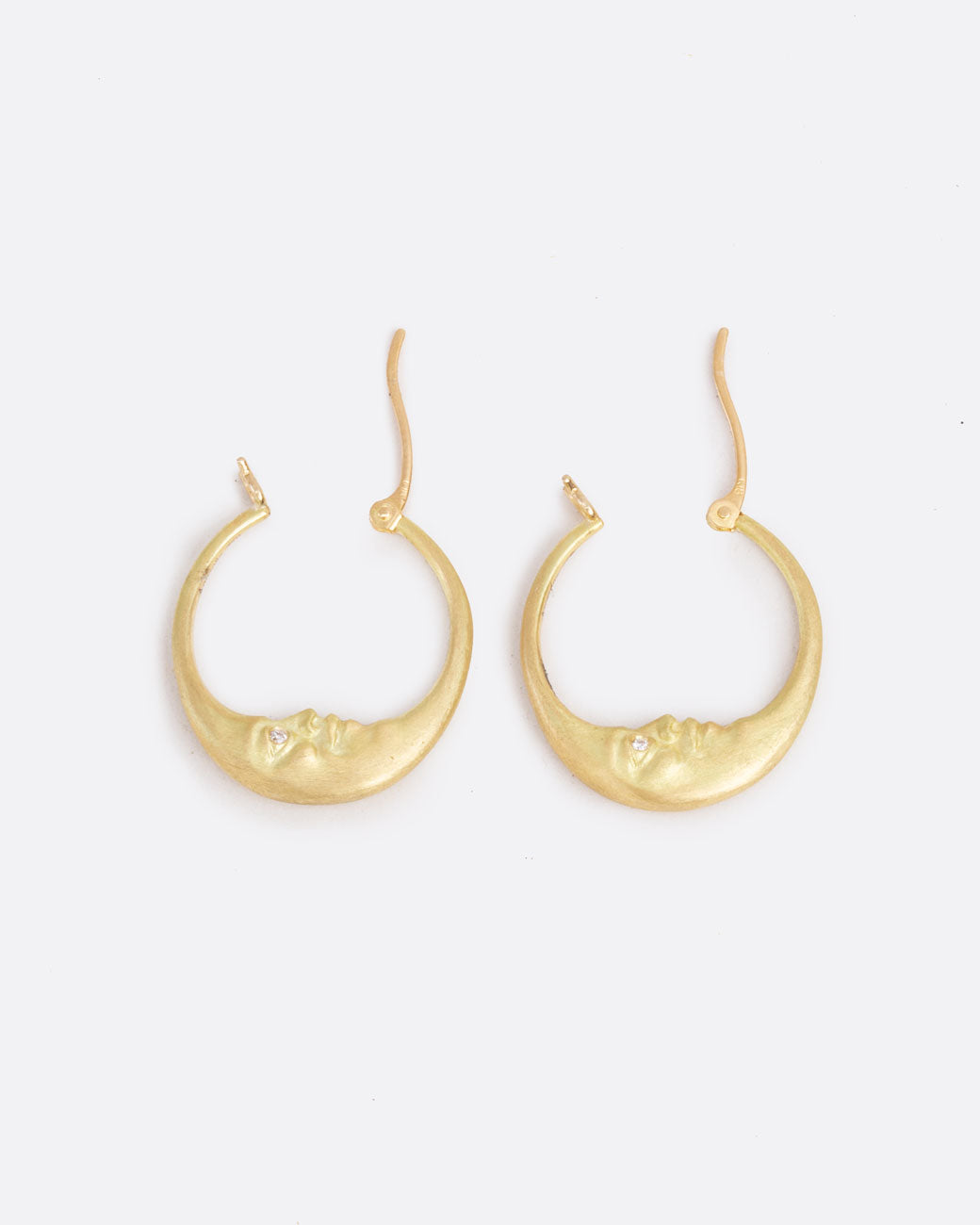 A pair of yellow gold crescent moon hoop earrings with faces and diamond eyes. Each hoop has a clasp at the top. Shown open from the side.