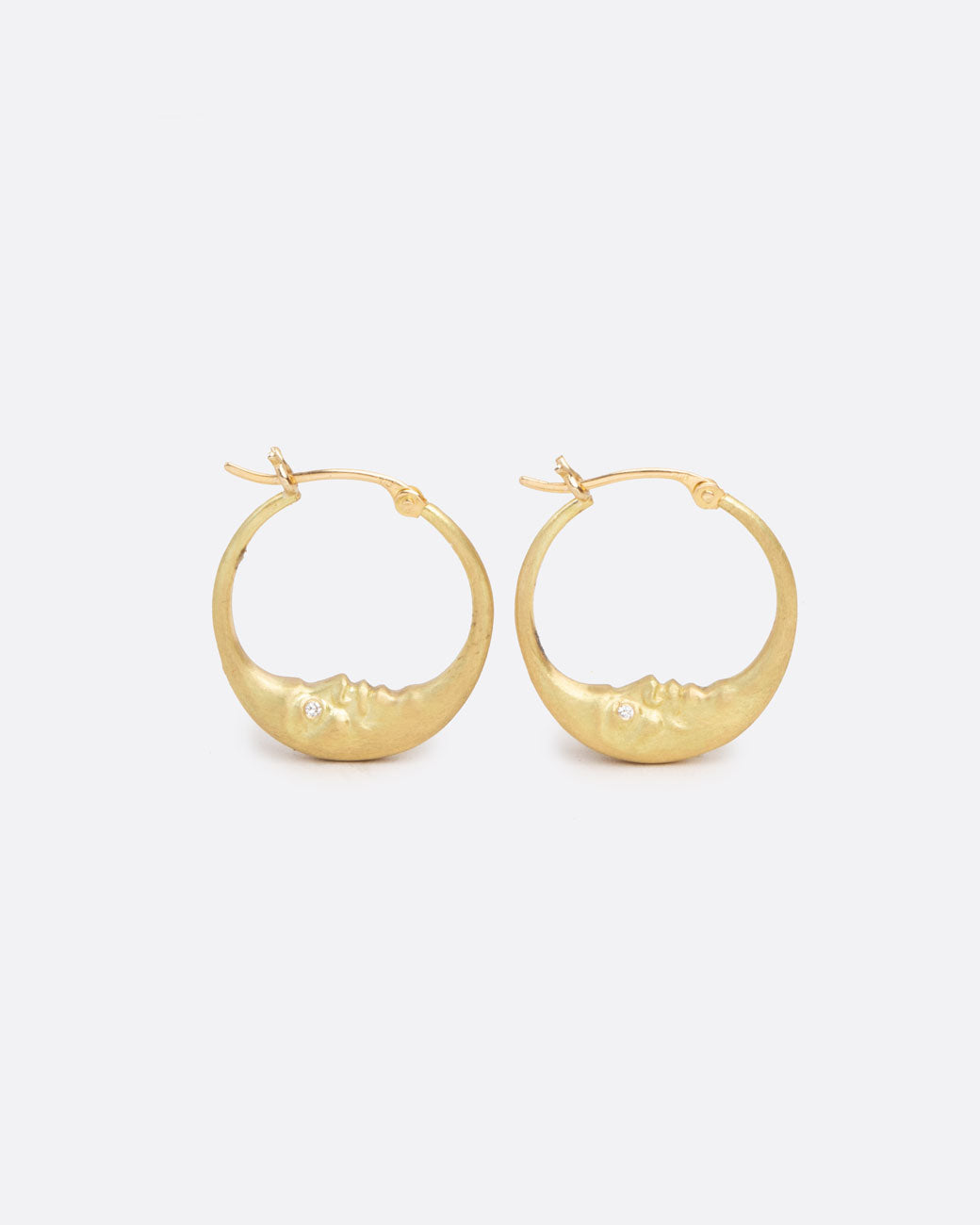A pair of yellow gold crescent moon hoop earrings with faces and diamond eyes. Each hoop has a clasp at the top. Shown from the side.