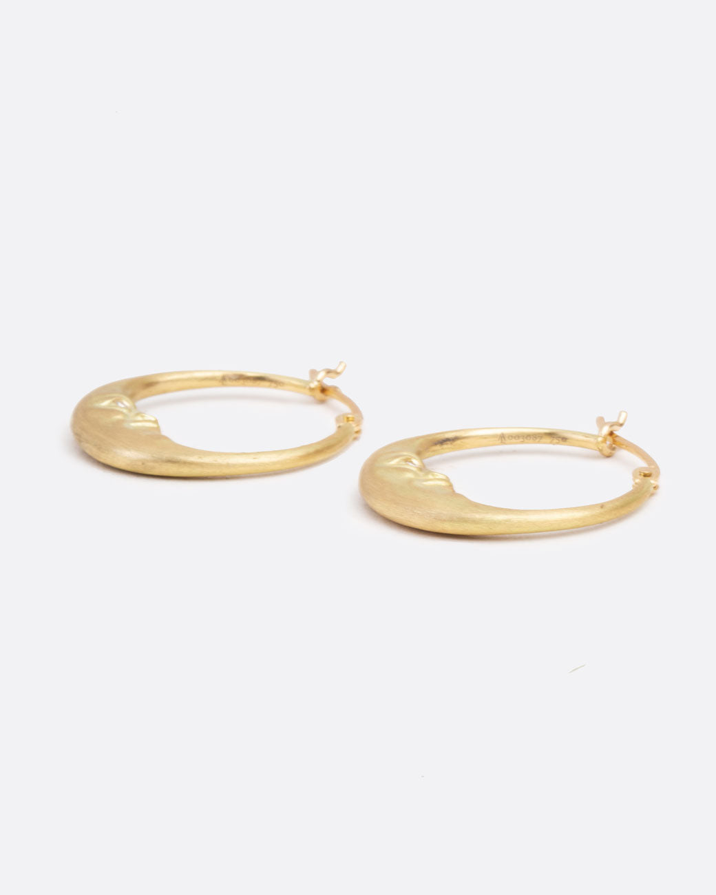 A pair of yellow gold crescent moon hoop earrings with faces and diamond eyes. Each hoop has a clasp at the top. Shown lying flat from the front.