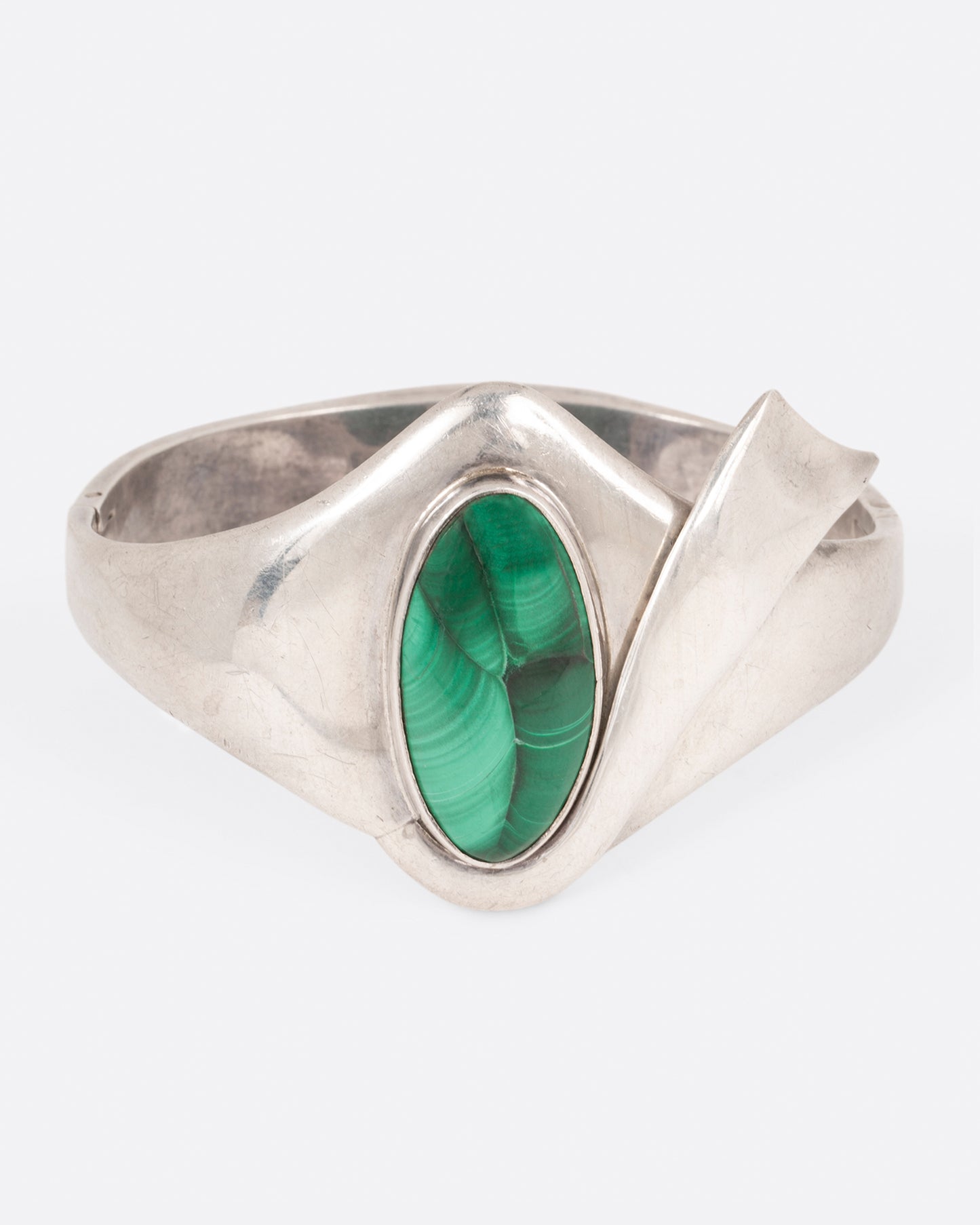 A sterling silver hinged bracelet with a large oval malachite at the center and a ribbon of silver draping off the side, shown from the front.