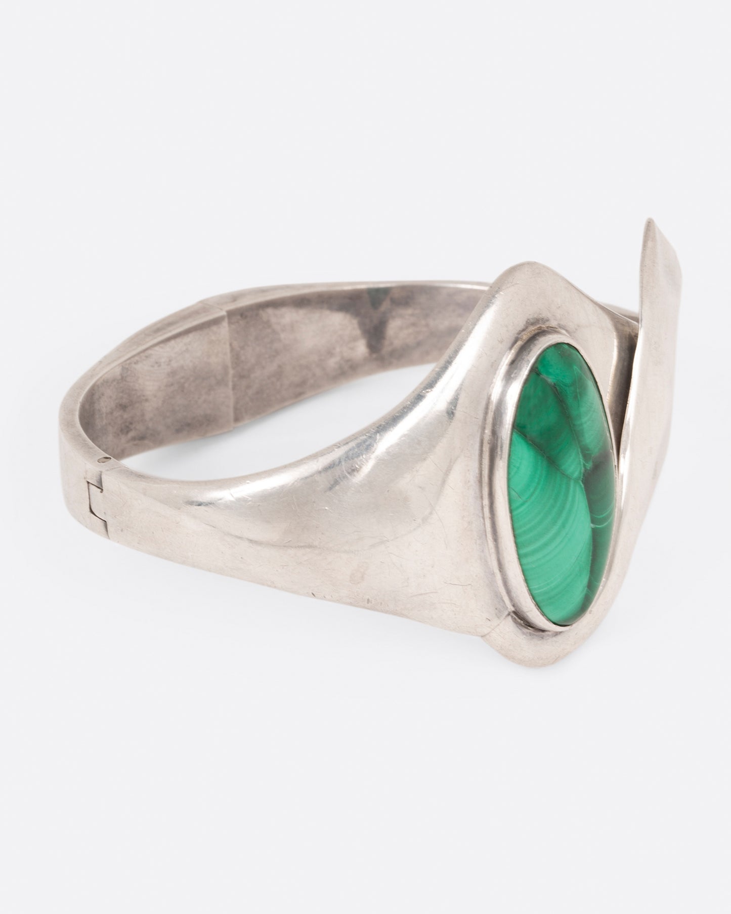 A sterling silver hinged bracelet with a large oval malachite at the center and a ribbon of silver draping off the side, shown from the side.