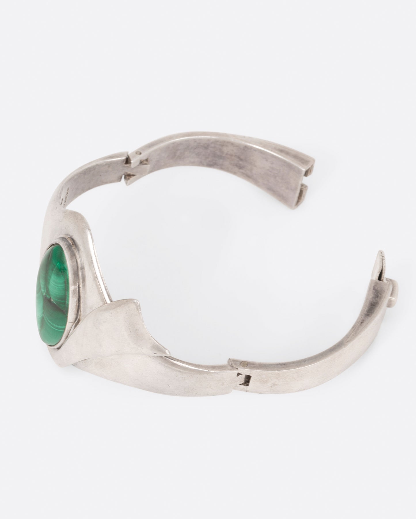 A sterling silver hinged bracelet with a large oval malachite at the center and a ribbon of silver draping off the side, shown open.