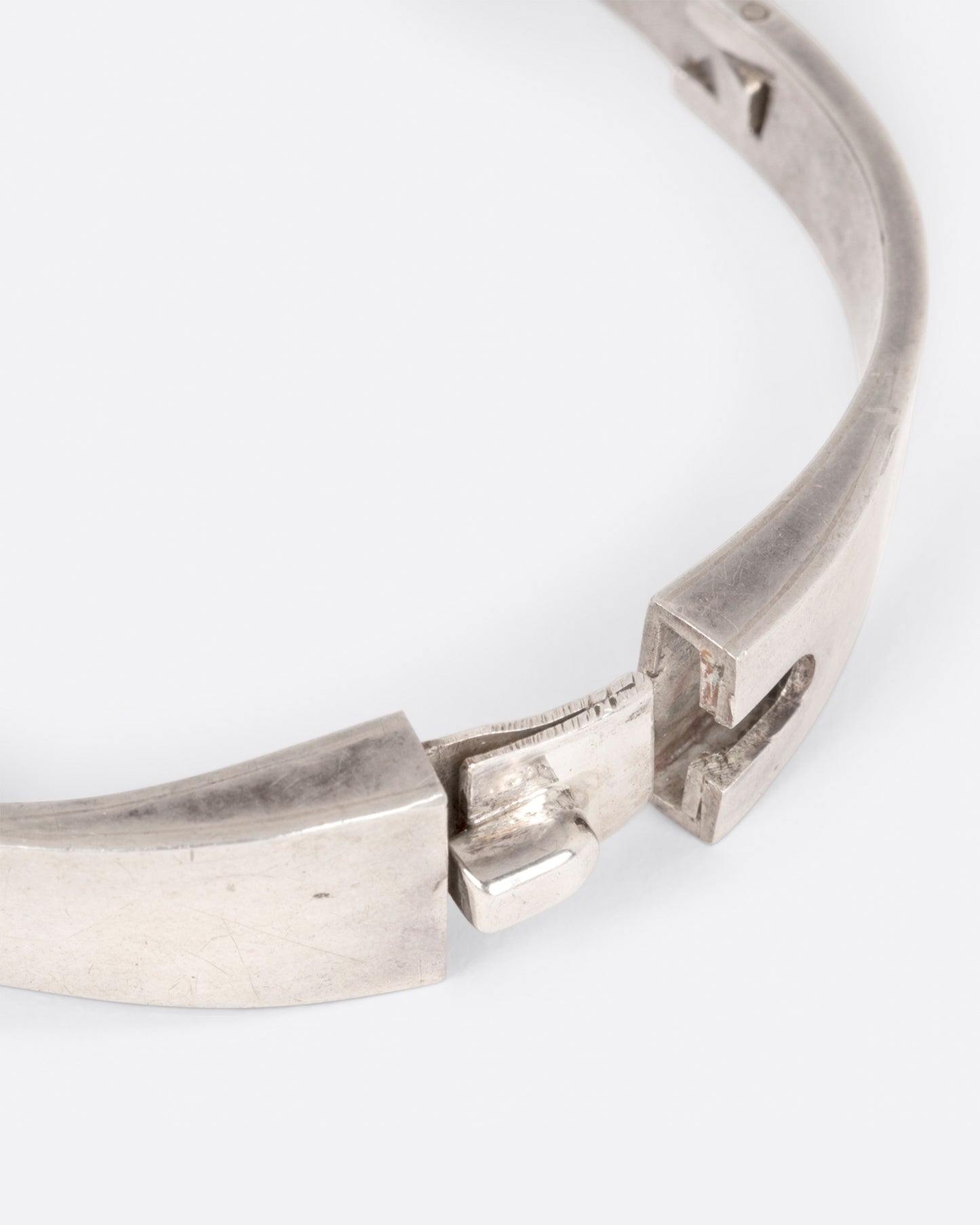 A close up of the clasp on a sterling silver hinged bracelet with a large oval malachite at the center and a ribbon of silver draping off the side.