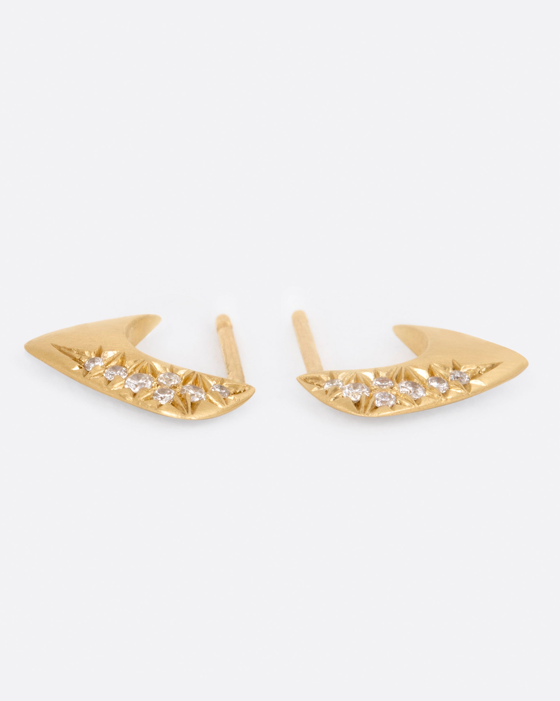 A pair of angular huggie hoop earrings with round pave diamonds on the outside of each, shown laying flat.