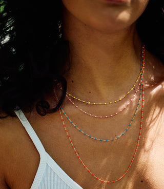 Four different length necklace, all in different colors, being worn layered together.