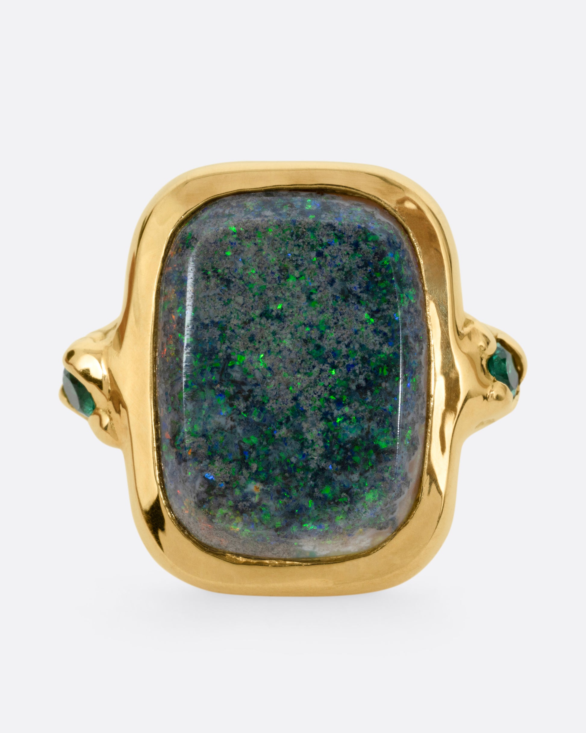 A yellow gold ring with a large rectangular boulder opal and emerald accents, shown from the front.