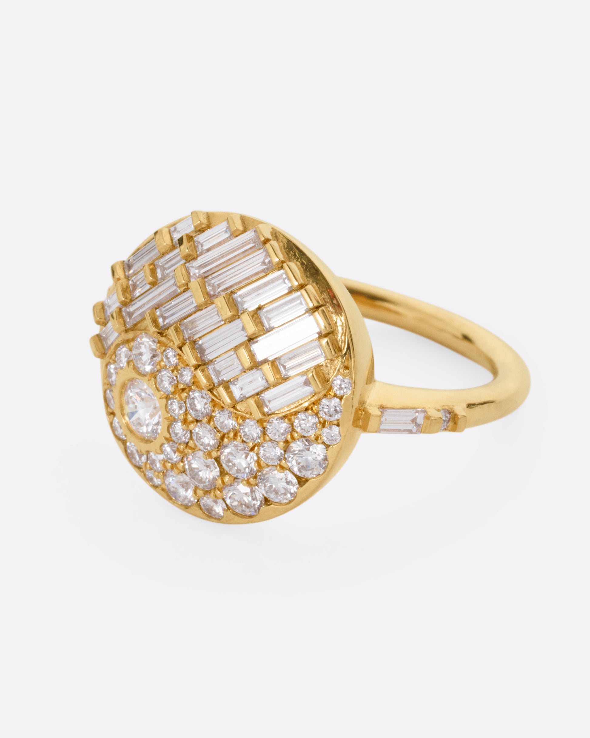 A yellow gold ring with a round face featuring a balance of brilliant round and baguette diamonds. Shown from the side.