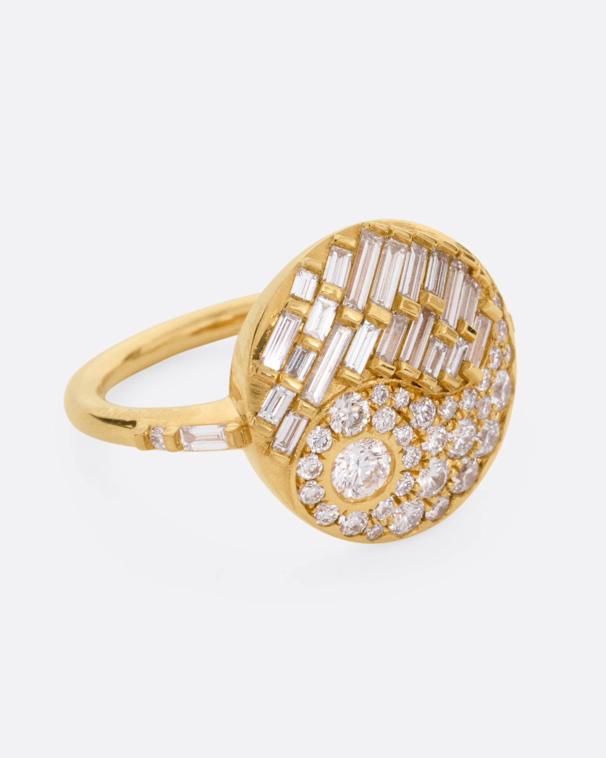 A yellow gold ring with a round face featuring a balance of brilliant round and baguette diamonds. Shown from the side.