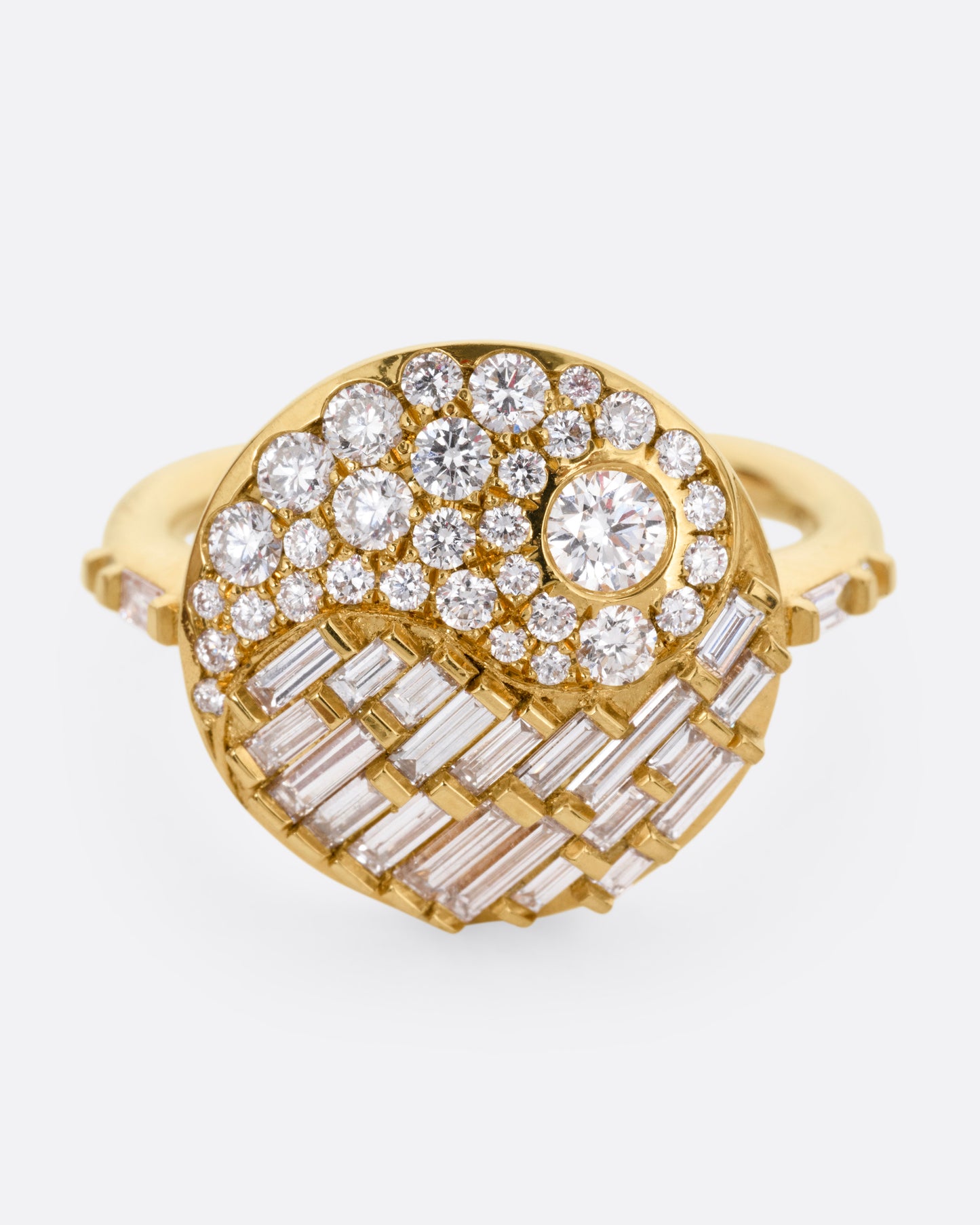 A yellow gold ring with a round face featuring a balance of brilliant round and baguette diamonds. Shown from the front.