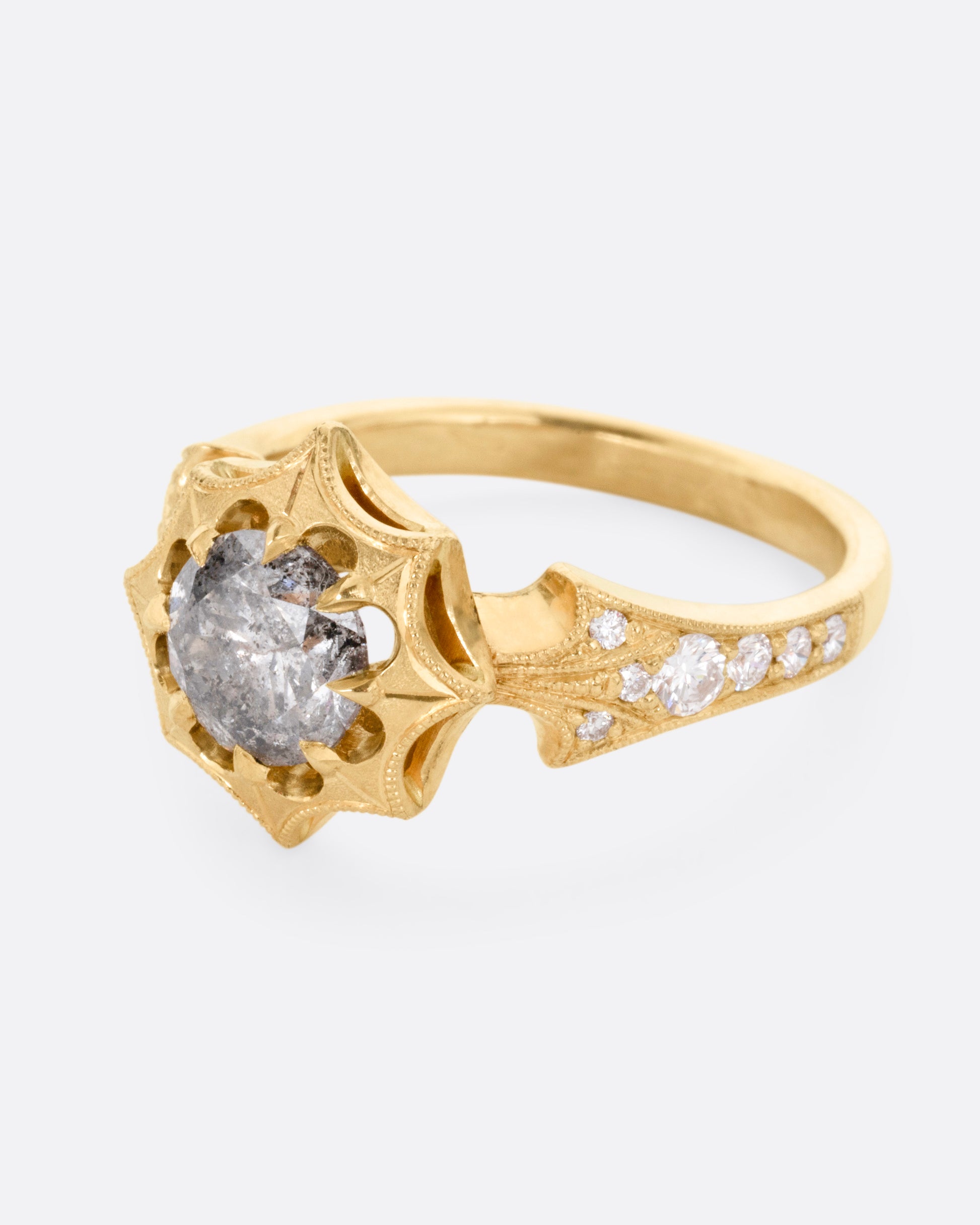 A yellow gold eight point starburst ring with a salt and pepper diamond in a prong setting, and diamond details on each shoulder, shown from the side.