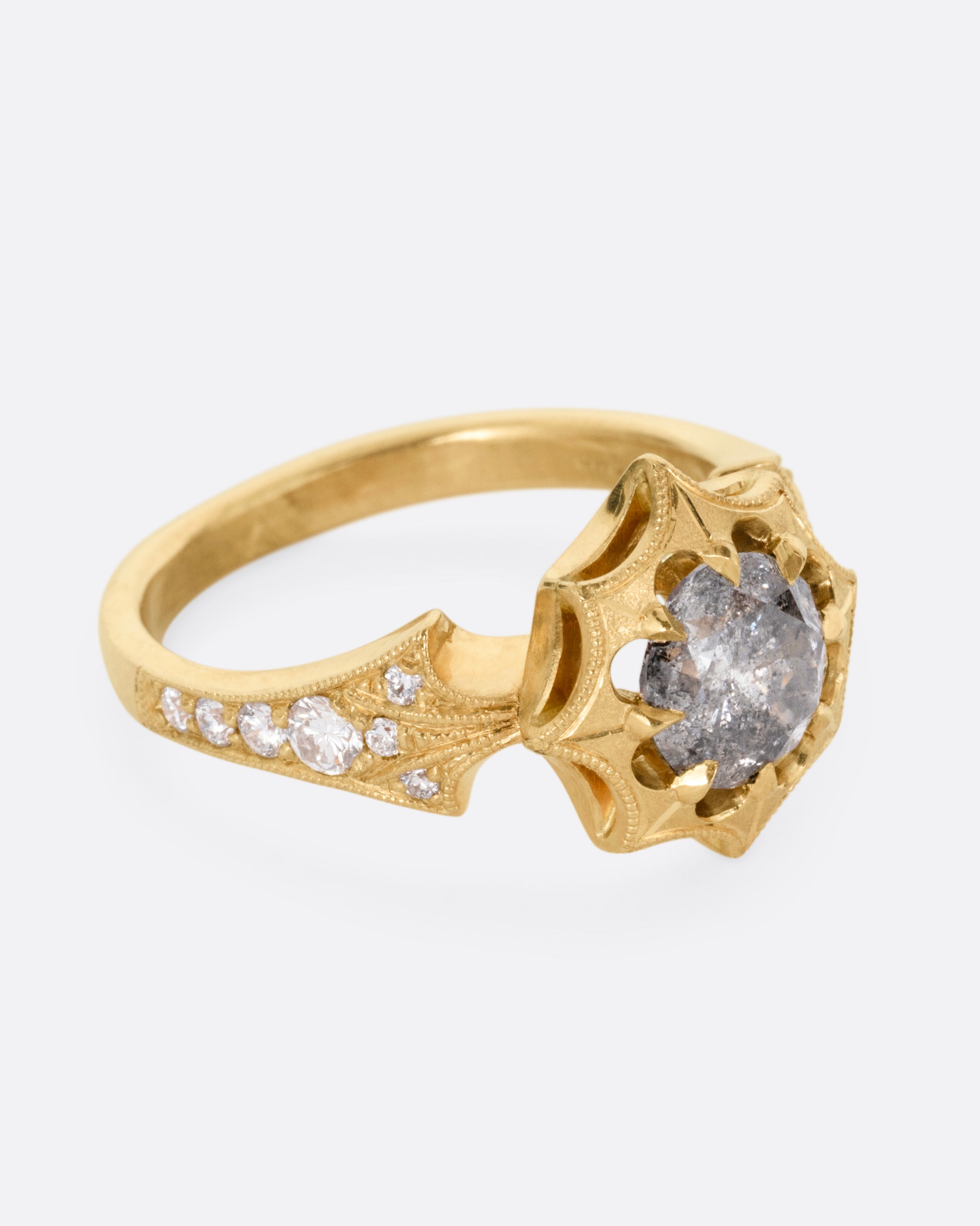 A yellow gold eight point starburst ring with a salt and pepper diamond in a prong setting, and diamond details on each shoulder, shown from the side.