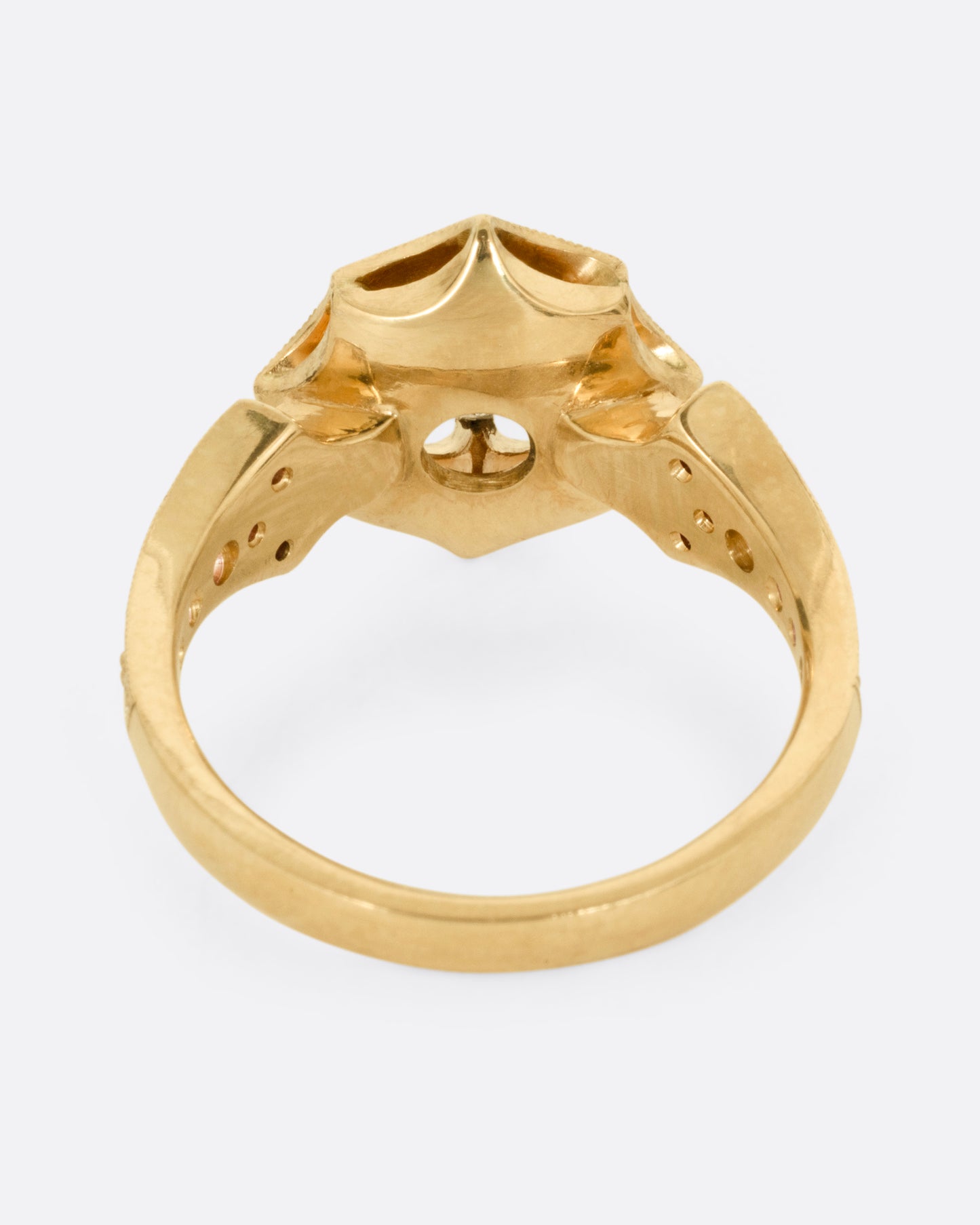 A yellow gold eight point starburst ring with a salt and pepper diamond in a prong setting, and diamond details on each shoulder, shown from the back.