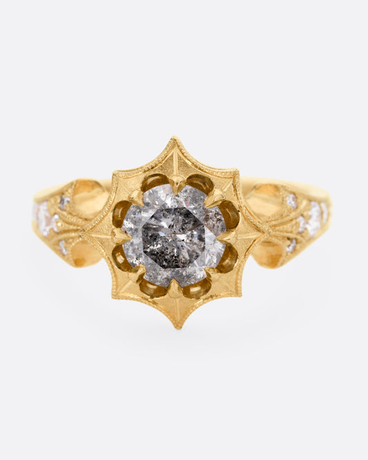 A yellow gold eight point starburst ring with a salt and pepper diamond in a prong setting, and diamond details on each shoulder, shown from the front.