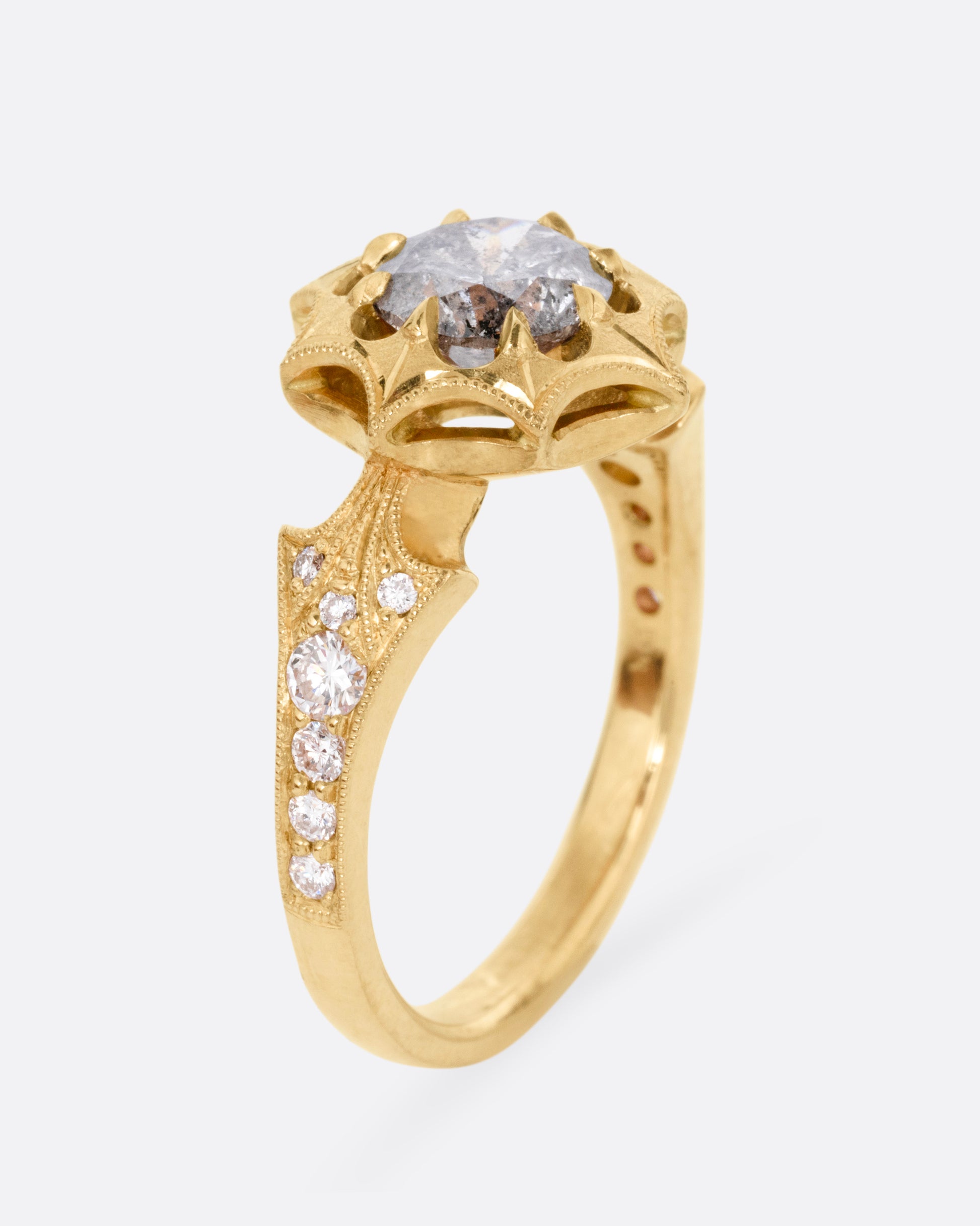A yellow gold eight point starburst ring with a salt and pepper diamond in a prong setting, and diamond details on each shoulder, shown from the side standing up. 