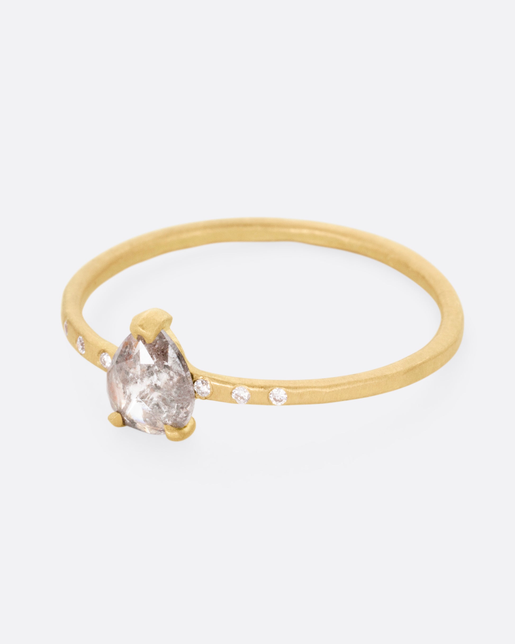 A yellow gold ring with a prong set salt and pepper diamond, flanked by tiny white diamond accents. Shown from the side.