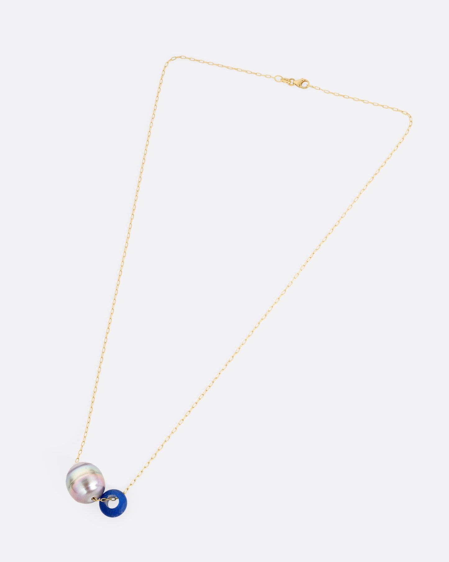 A yellow gold cable chain necklace with a blue glass antique bead and a Tahitian pearl, shown from the front.