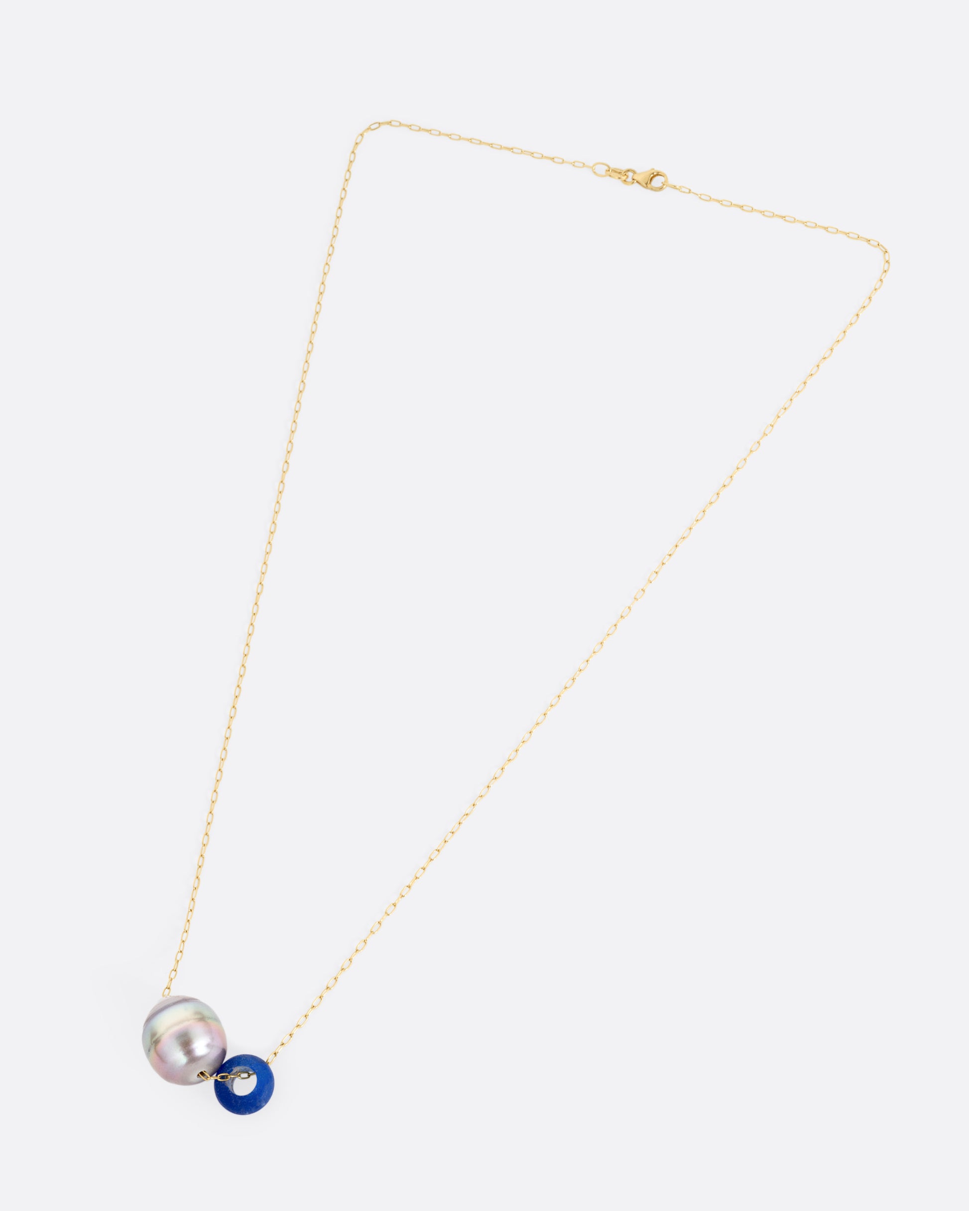 A yellow gold cable chain necklace with a blue glass antique bead and a Tahitian pearl, shown from the front.