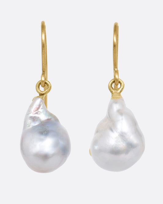 A pair of pearl earrings with yellow gold ear hooks, shown from the front.