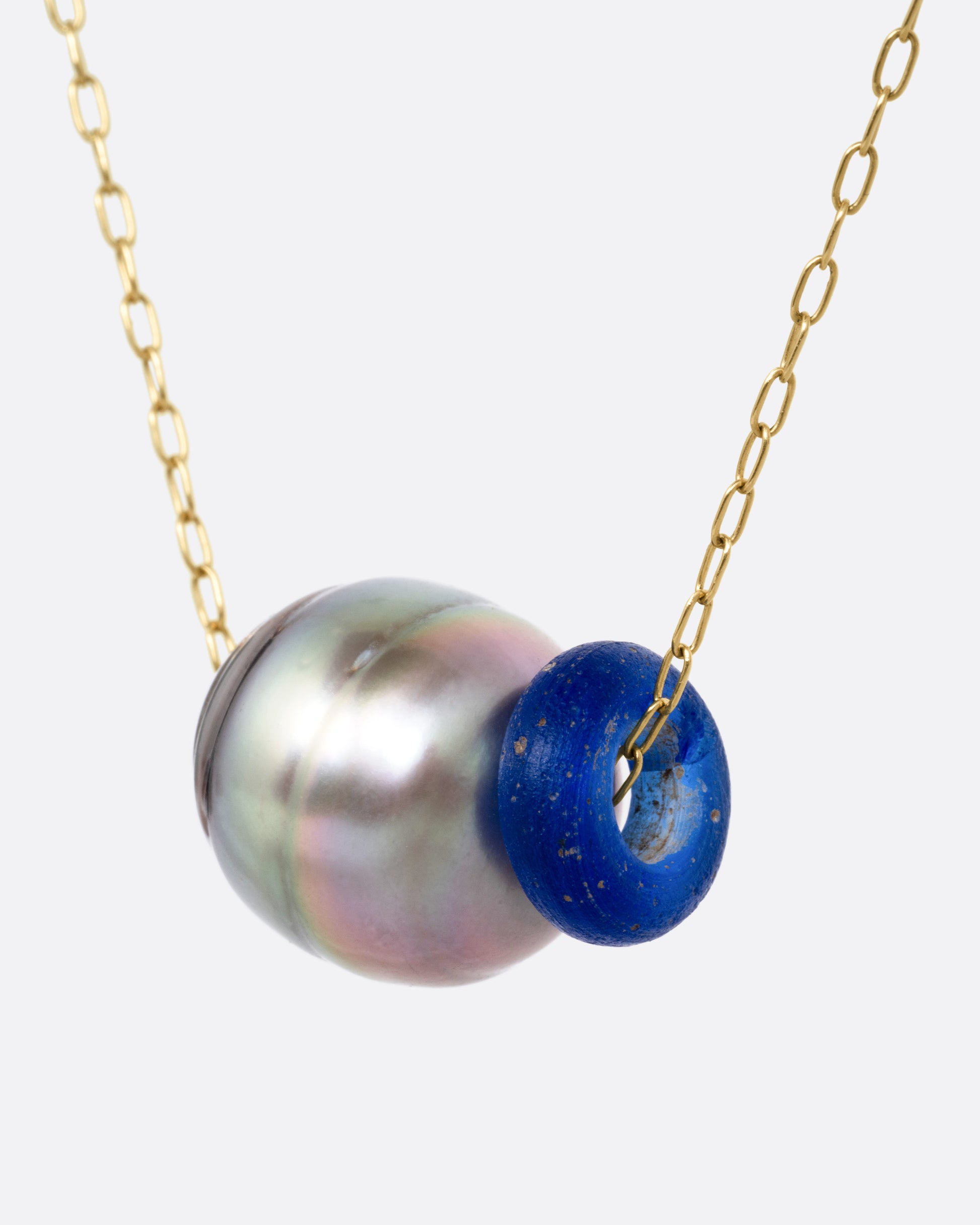 A yellow gold cable chain necklace with a blue glass antique bead and a Tahitian pearl, shown from the side.