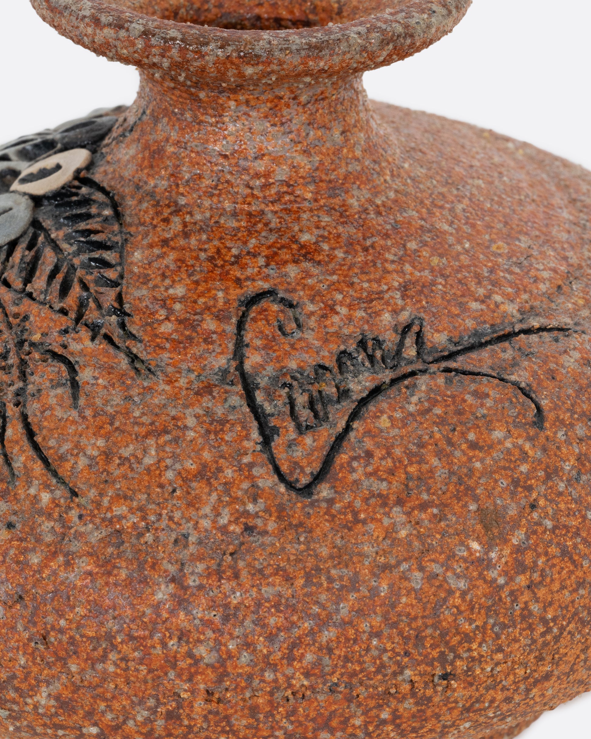 A brown stoneware pottery vase with a floral motif on the side. Signature shown close up.