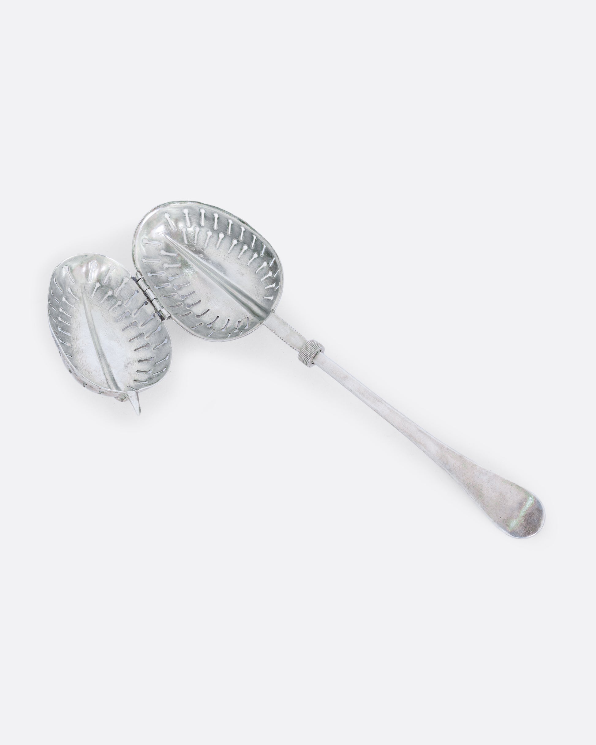 A sterling silver spoon tea infuser with a screw mechanism. Shown open.