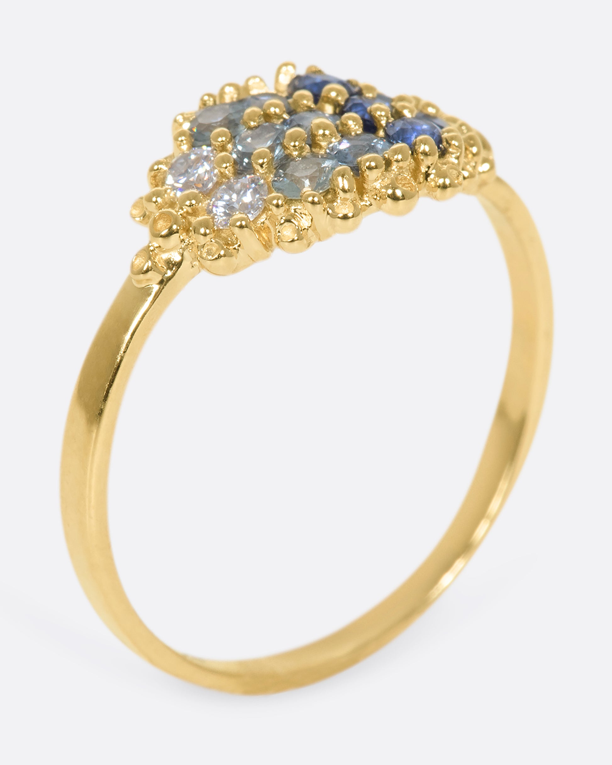 A view of a yellow gold ring with 12 sapphires in a range of blue shades standing upright on its band.