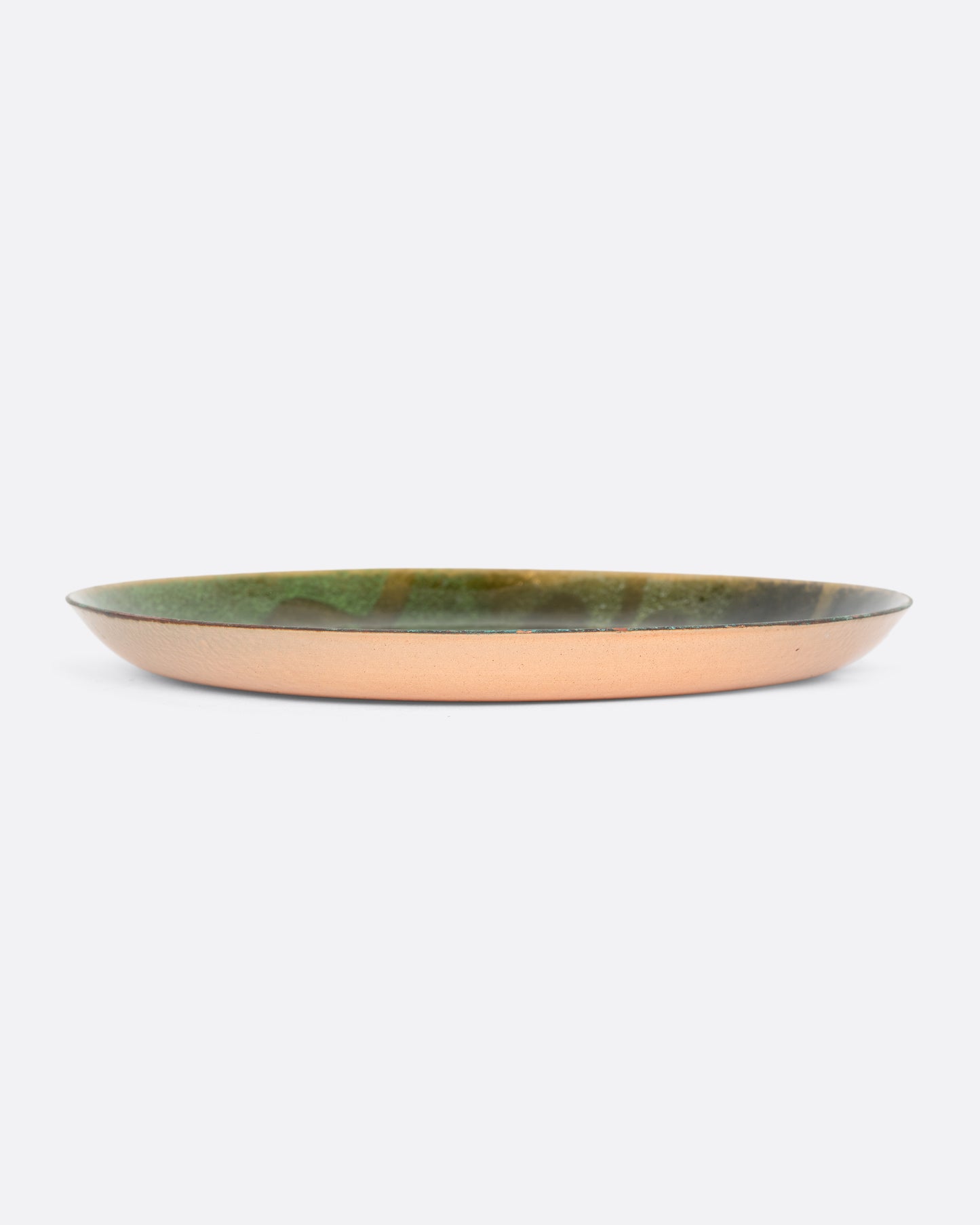 A small gradient green enameled metal plate with a leaf motif. Shown sitting on a table.