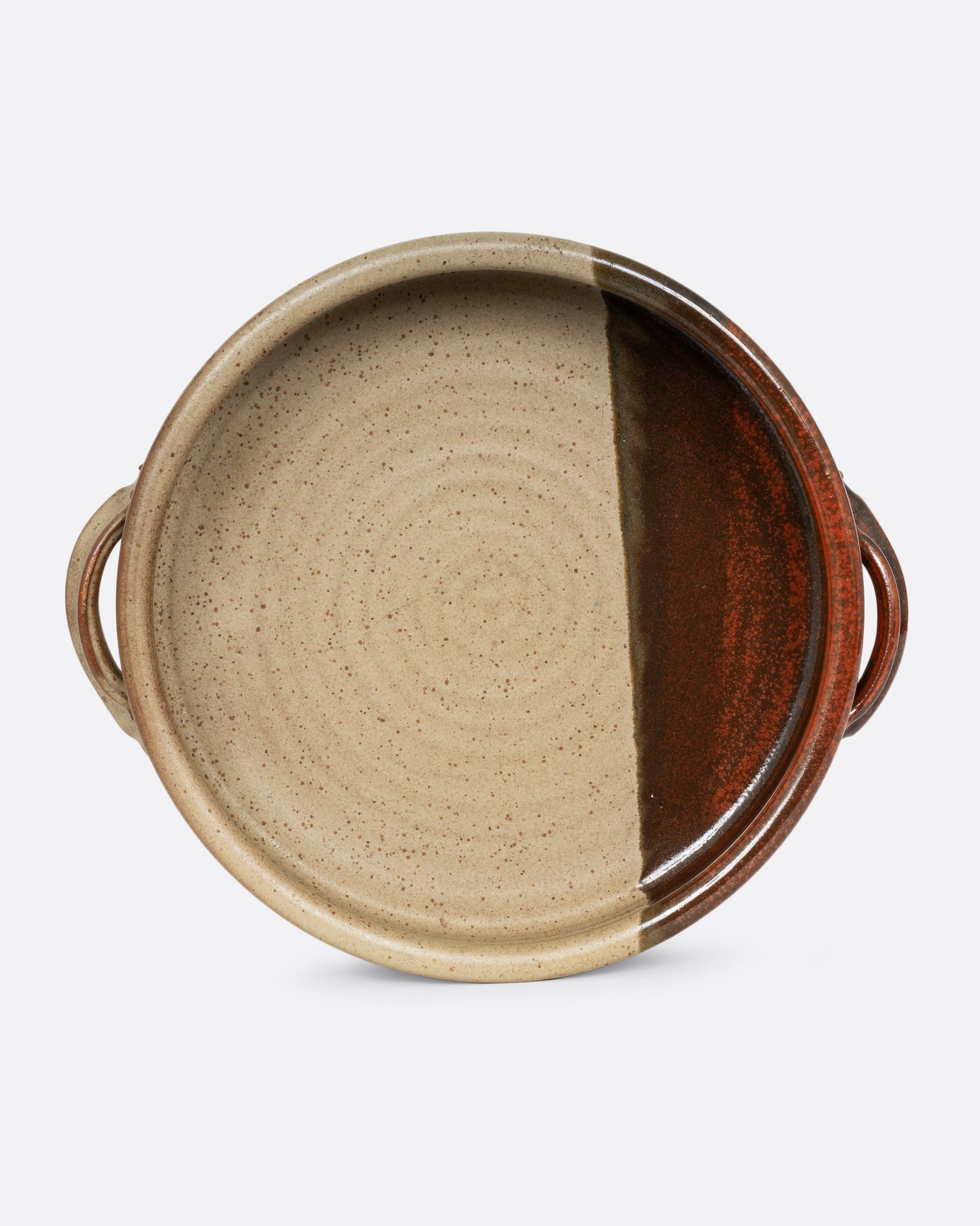 A handled serving bowl with a dipped brown glaze on one side. Shown from the front standing up.