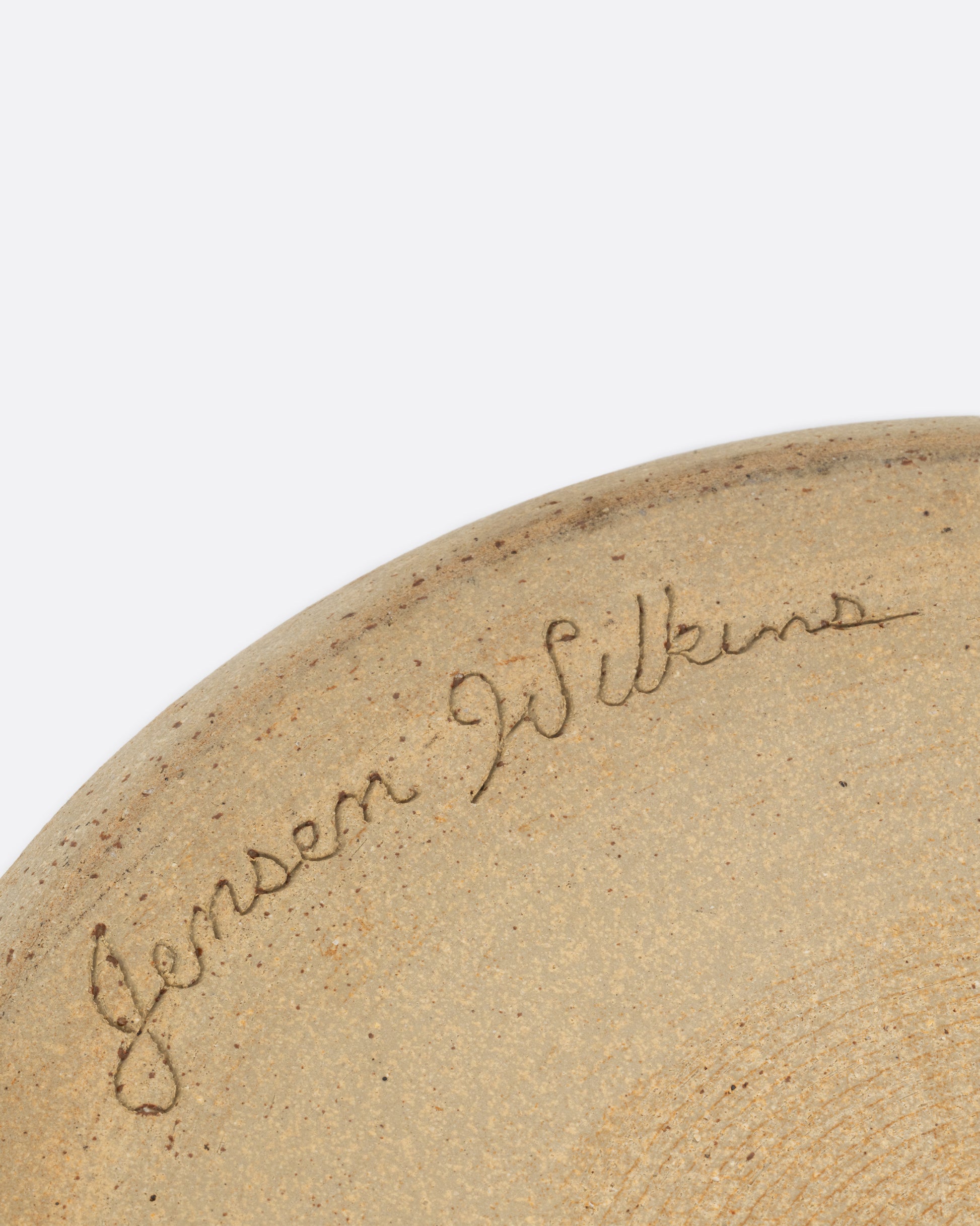 A close up of the artist's signature on the backside of a handled serving bowl. Shown from the back.