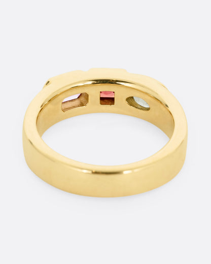 A yellow gold band with three mixed cut multicolored sapphires. Shown from the back.