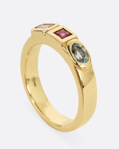 A yellow gold band with three mixed cut multicolored sapphires. Shown from the side standing up.