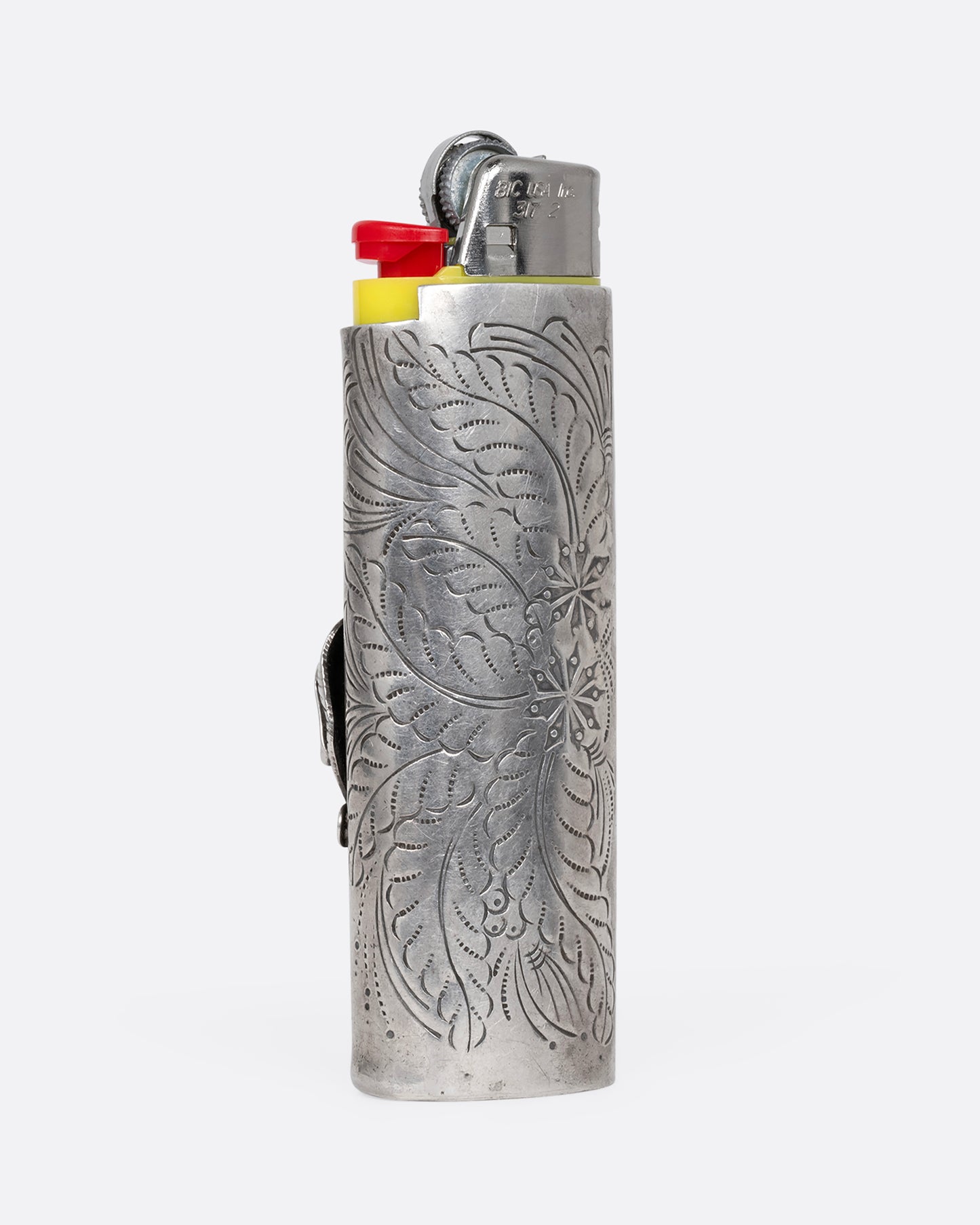 A sterling silver lighter with hand engraved botanical motif, shown from the back holding a yellow contemporary lighter.