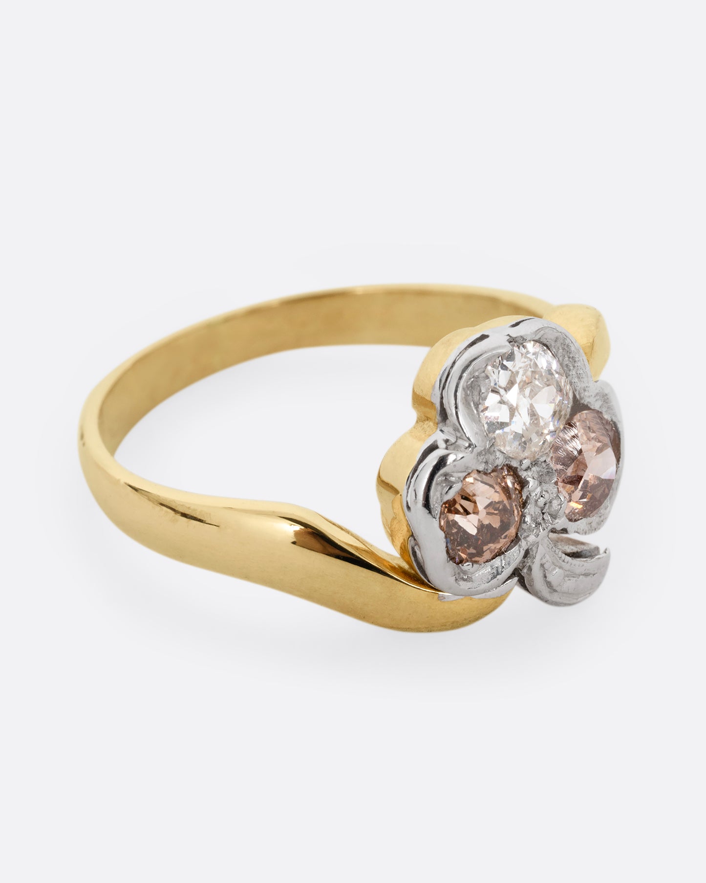 A yellow gold ring with a white gold three leaf clover at the center, made of white and cognac diamonds. Shown from the side.