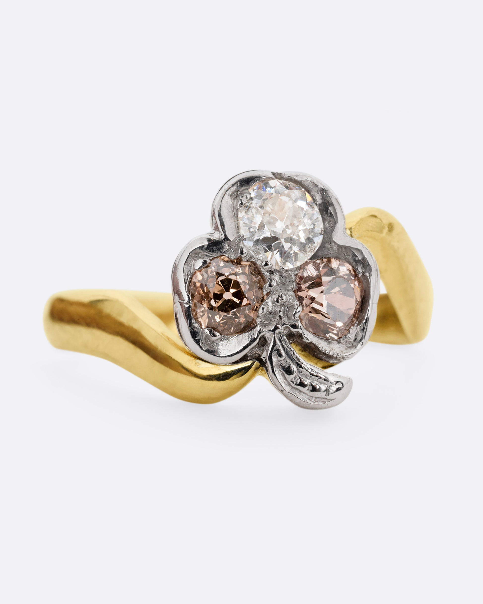 A yellow gold ring with a white gold three leaf clover at the center, made of white and cognac diamonds. Shown from the front.