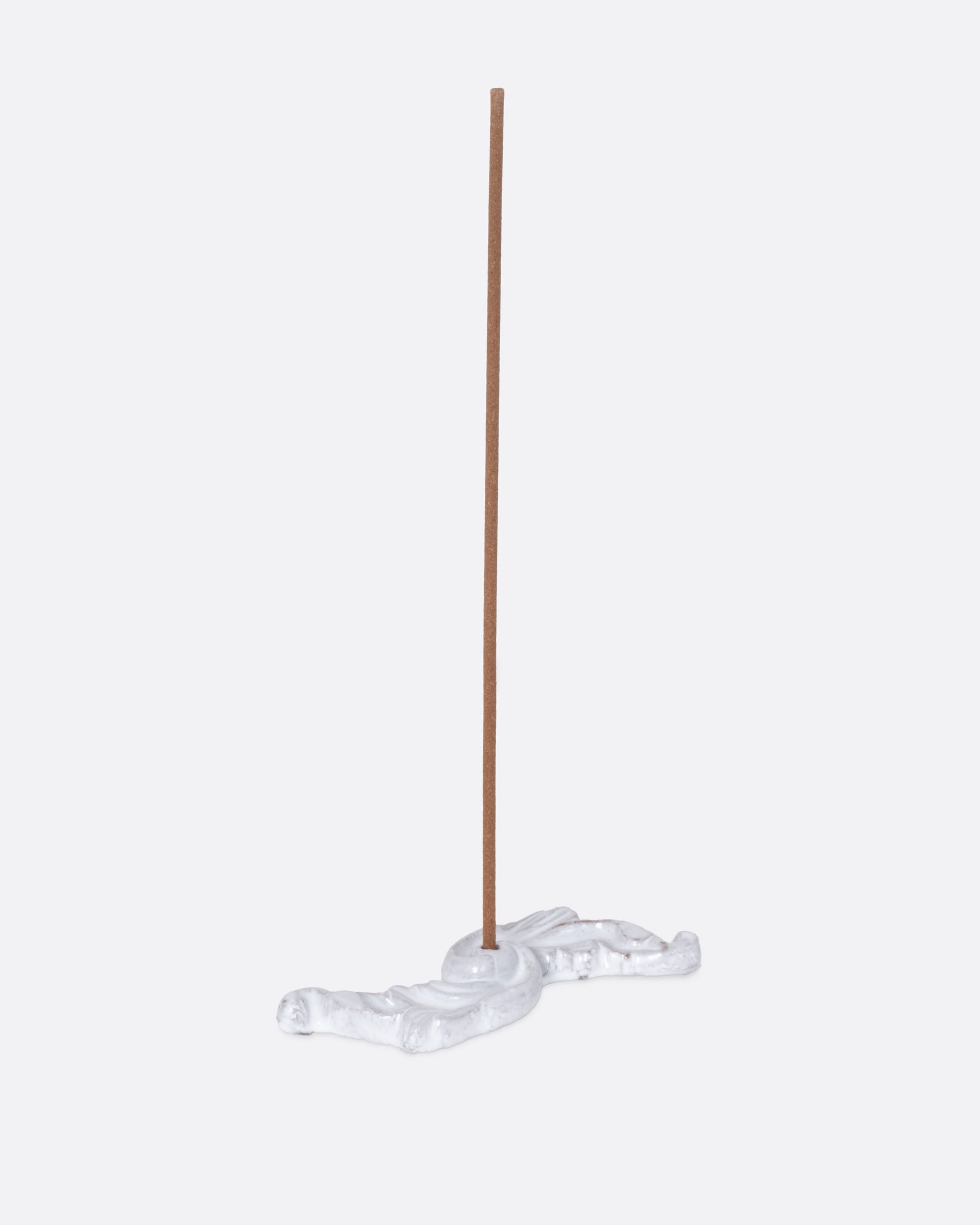A white ceramic floral shaped incense burner, shown from the side with an incense stick in it.