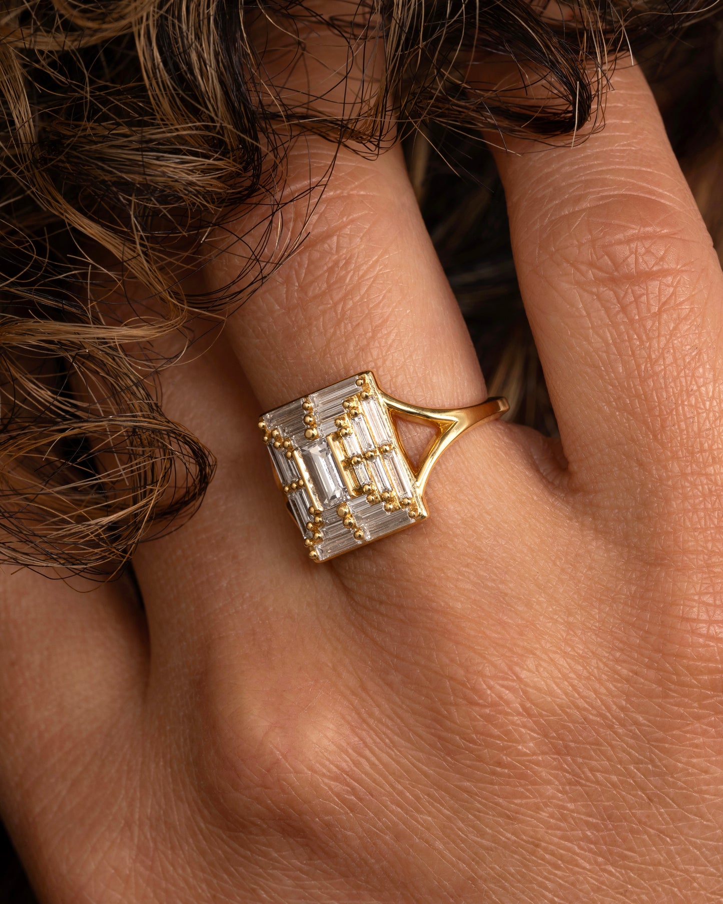 A yellow gold ring with a mosaic of white diamonds in the shape of a square. Shown  worn on a hand.