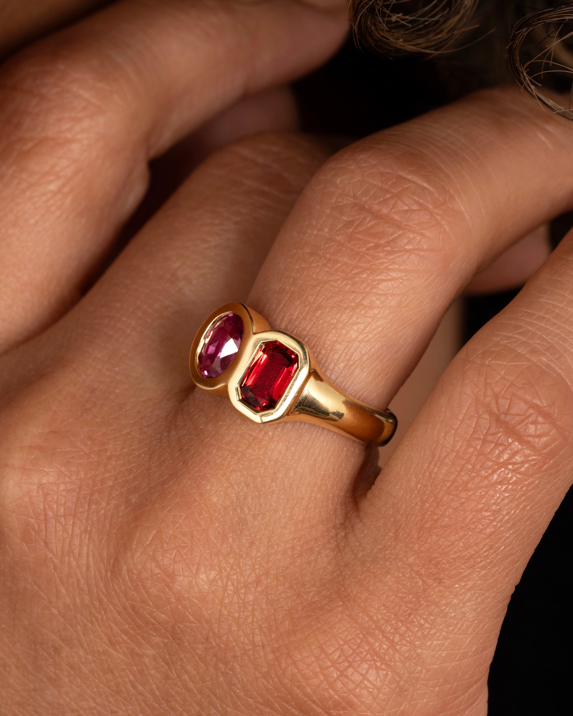 yellow gold ring with red and orange sapphires shown worn on a hand