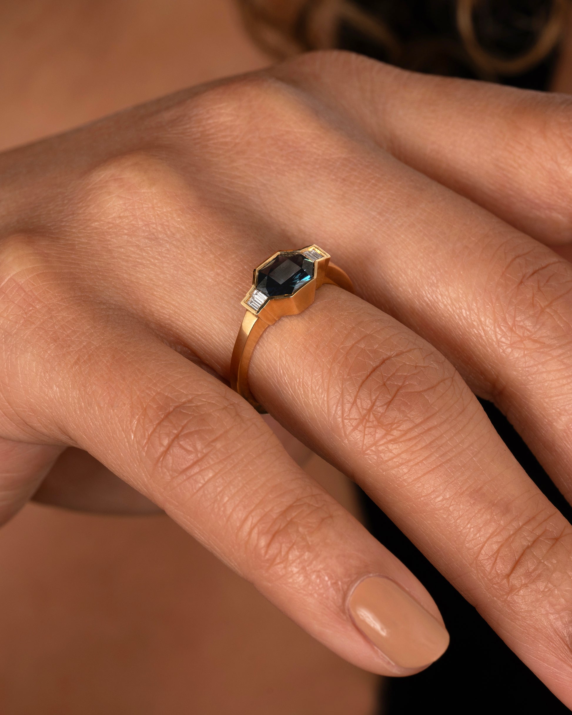 A yellow gold ring with a sapphire at the center and baguette diamonds on either side. Shown worn on a hand.