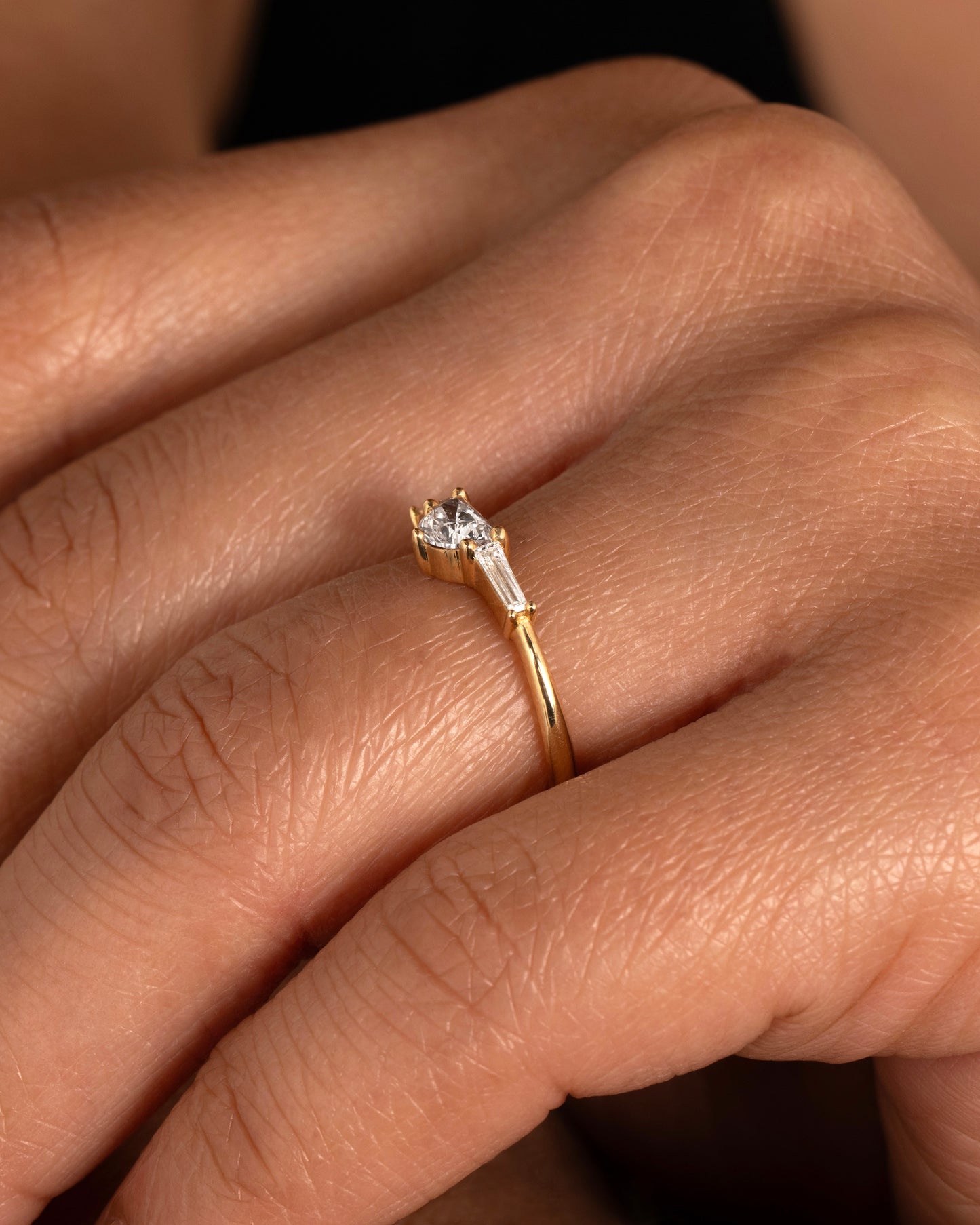 A yellow gold ring with a half moon shaped diamond and two baguette diamonds. Shown on a hand.