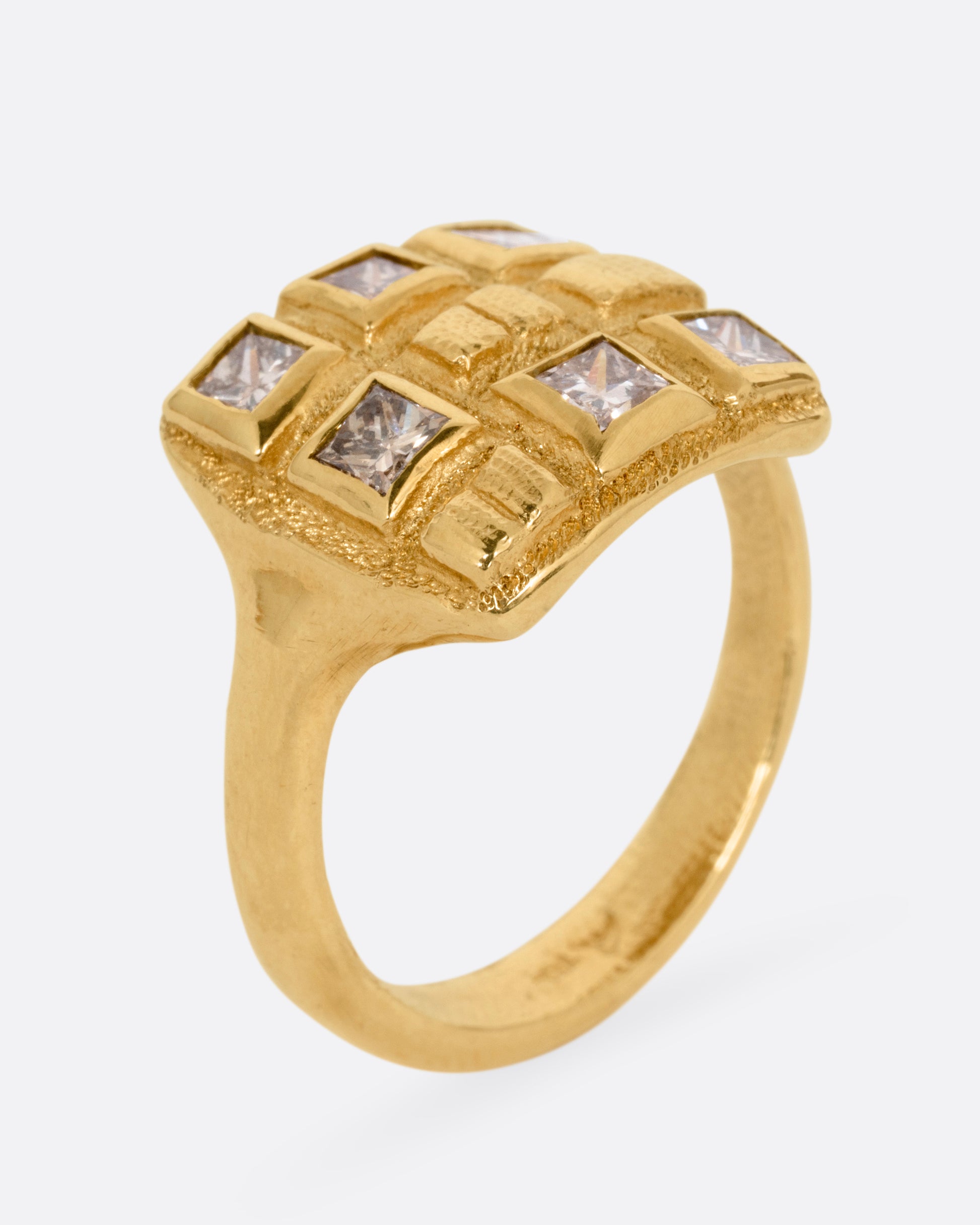 A yellow gold ring with princess cut brown diamonds and raised textural squares across its broad face. Shown from the side standing up.