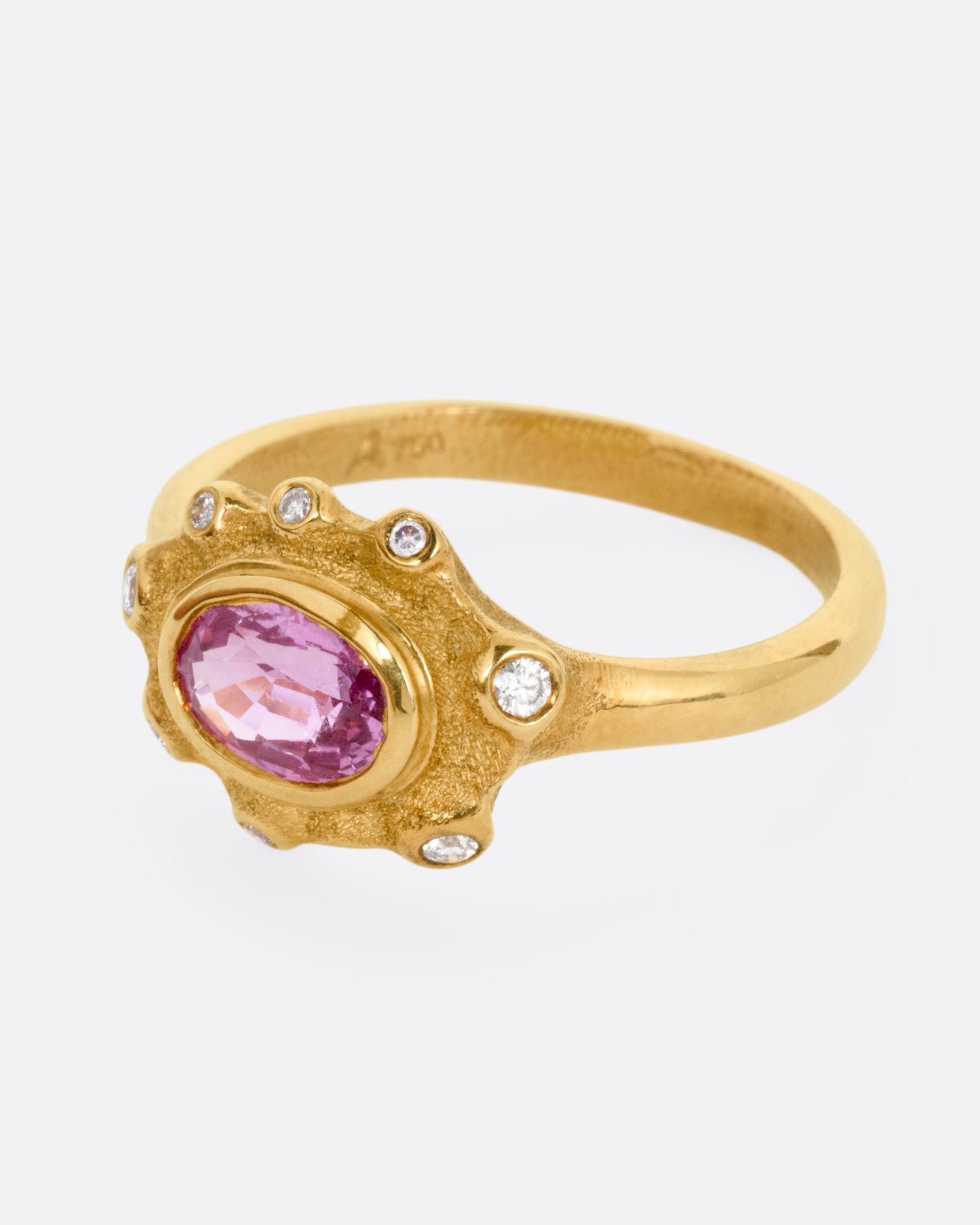 A yellow gold band with a halo of white diamonds surrounding a pink sapphire, shown from the side.