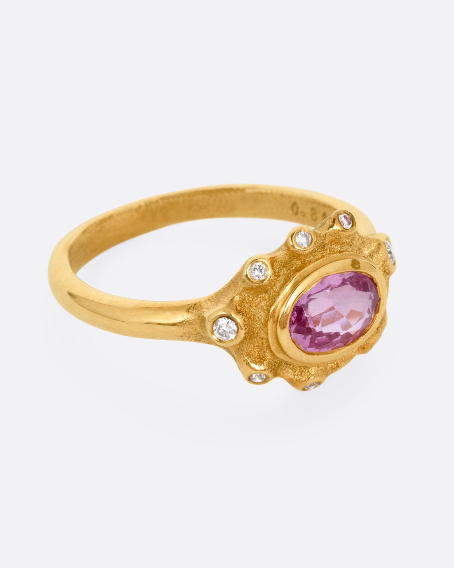 A yellow gold band with a halo of white diamonds surrounding a pink sapphire, shown from the side.