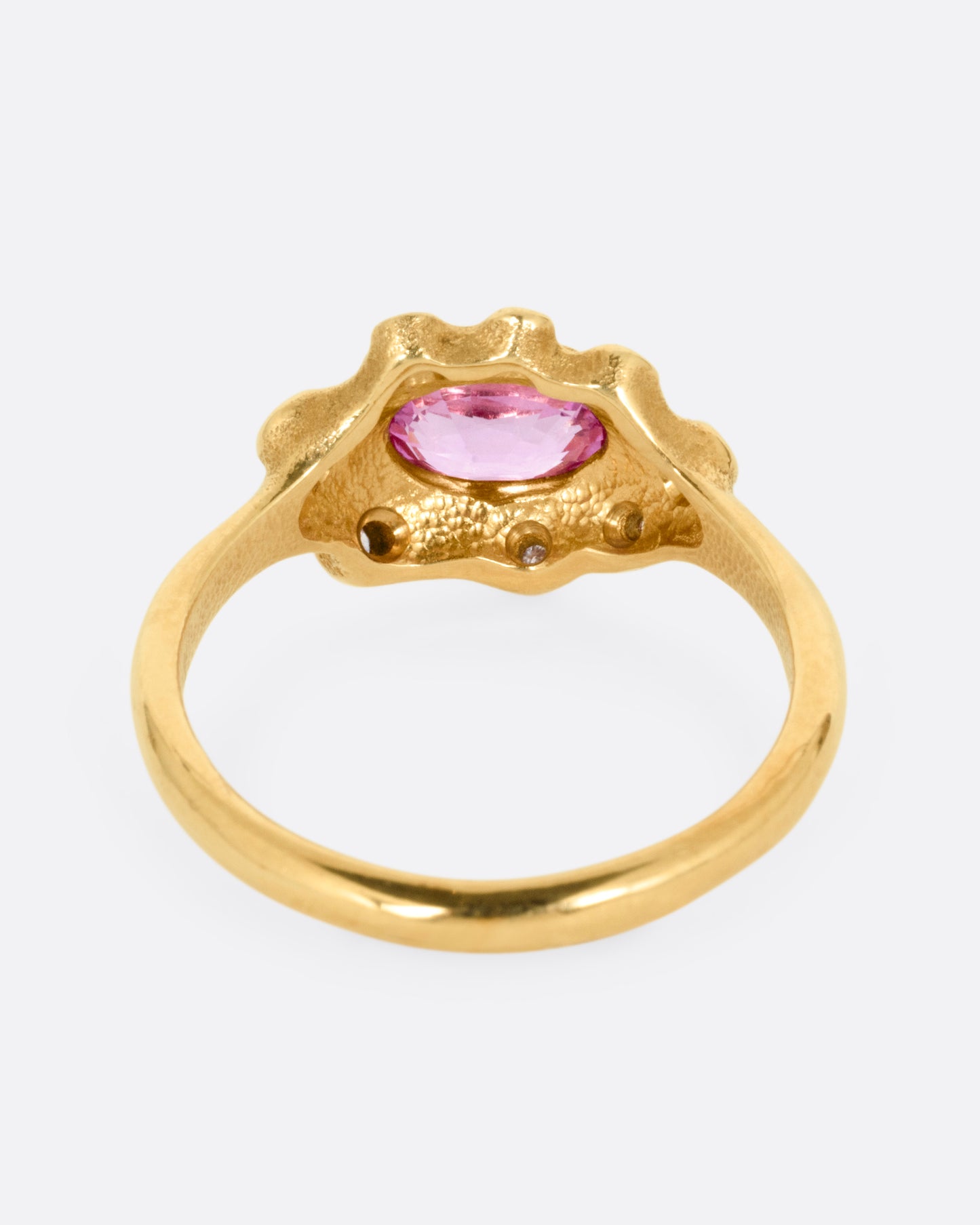 A yellow gold band with a halo of white diamonds surrounding a pink sapphire, shown from the back.