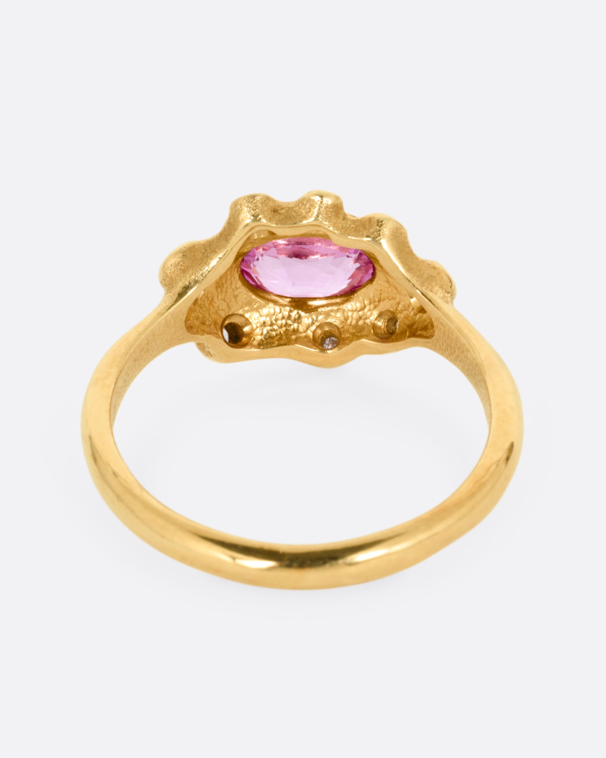 A yellow gold band with a halo of white diamonds surrounding a pink sapphire, shown from the back.