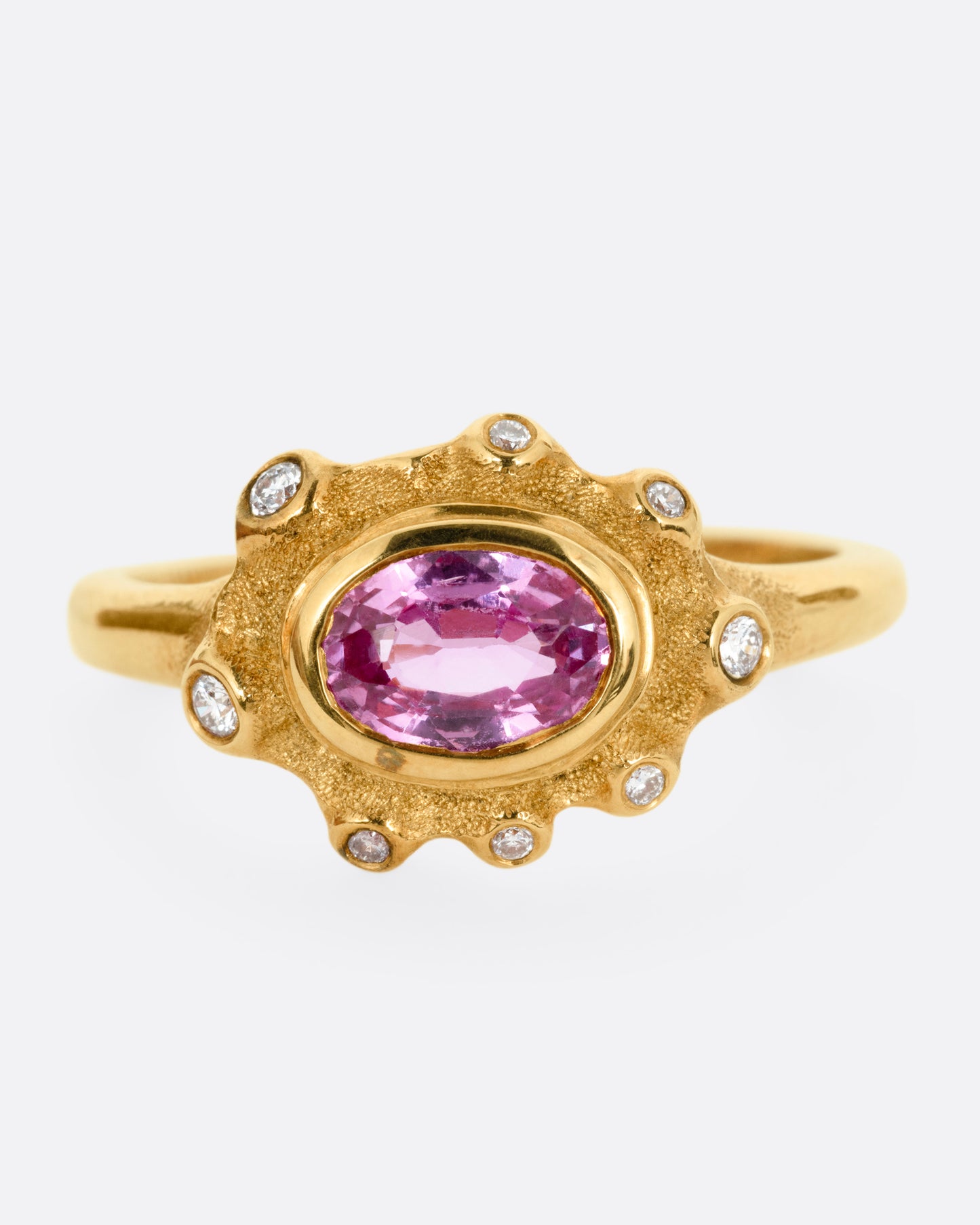 A yellow gold band with a halo of white diamonds surrounding a pink sapphire, shown from the front.
