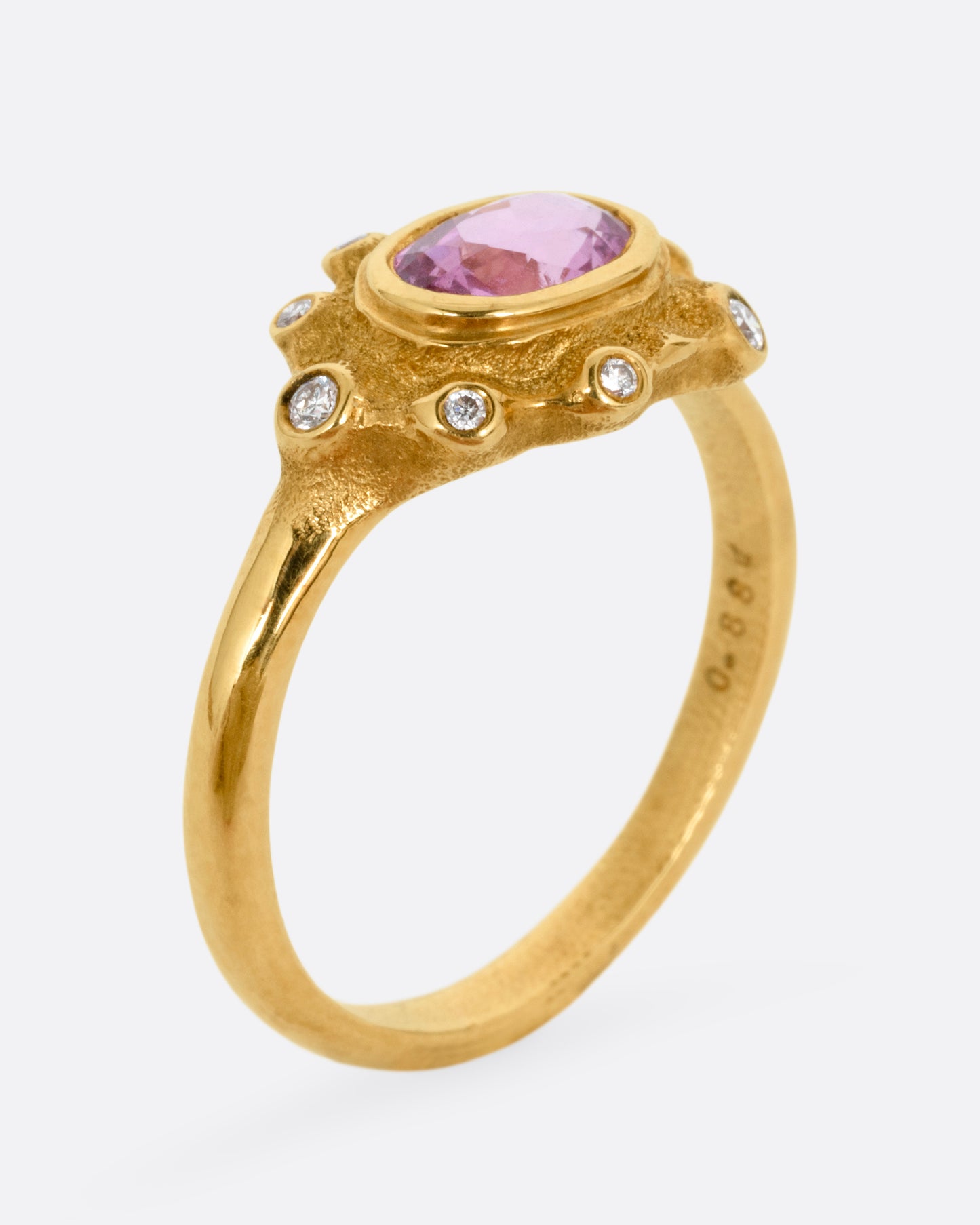 A yellow gold band with a halo of white diamonds surrounding a pink sapphire, shown from the side standing up.