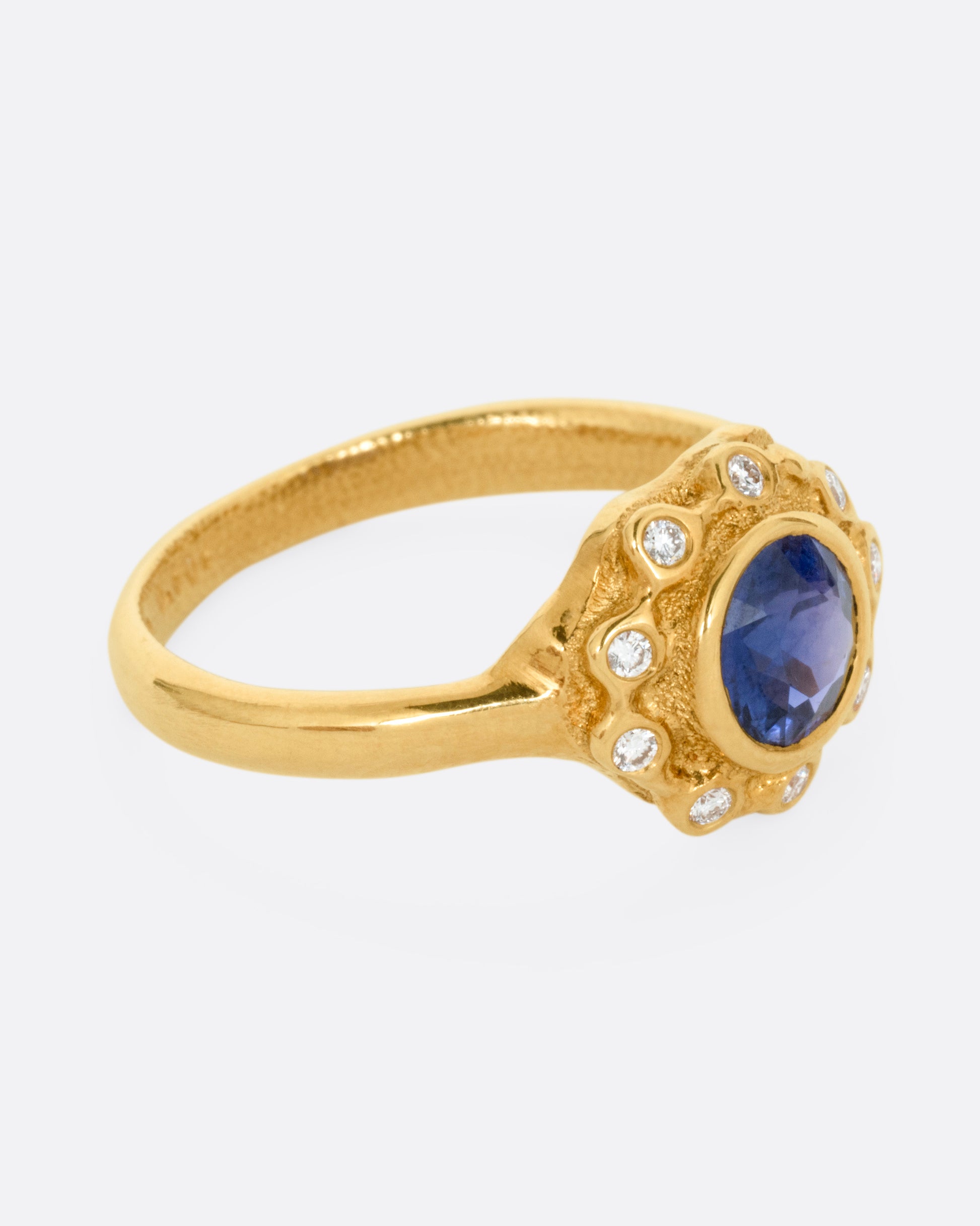 A yellow gold ring with a halo of white diamonds around a sapphire, shown from the side.
