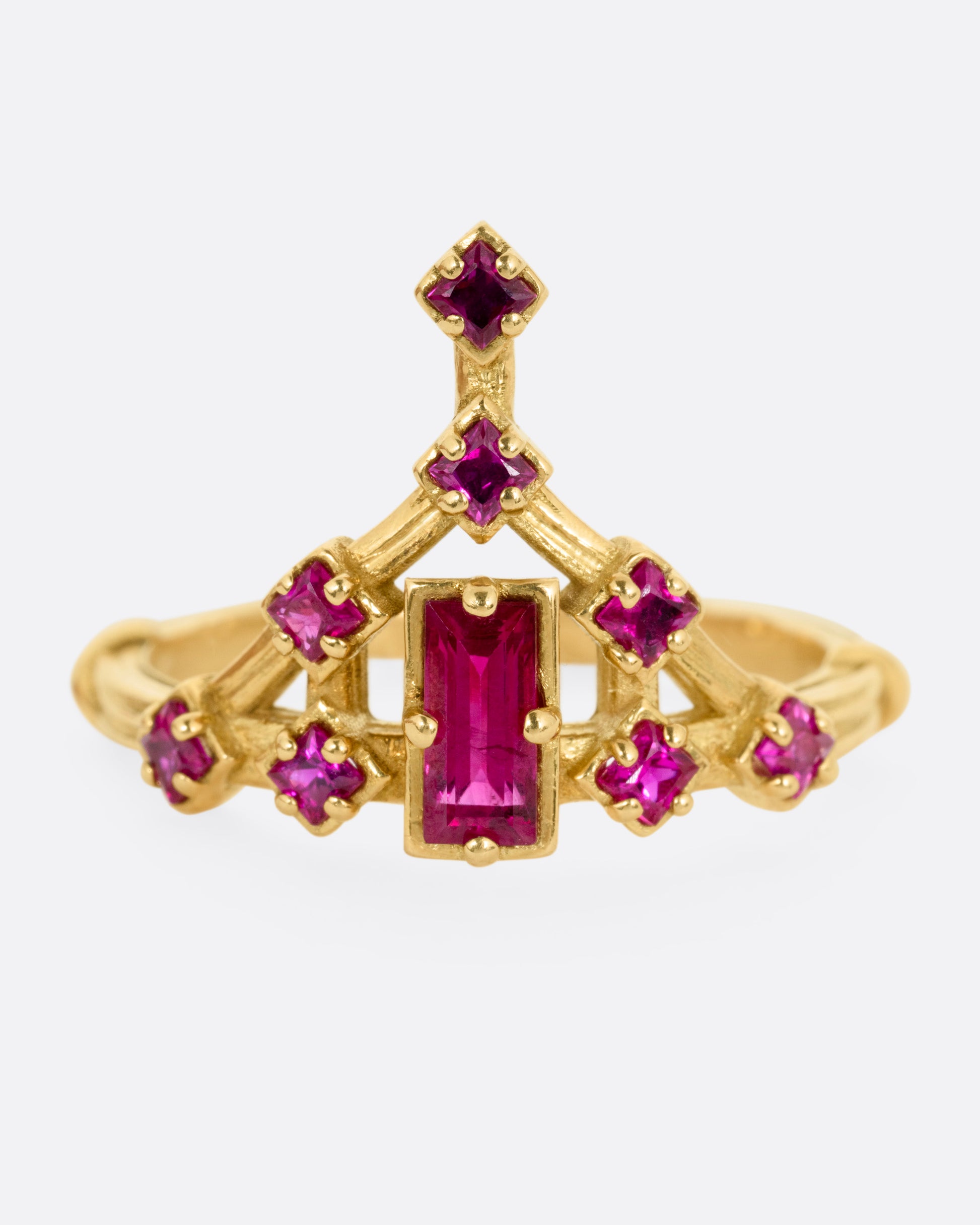A yellow gold ring with a baguette ruby and princess cut ruby accents. Shown from the front.