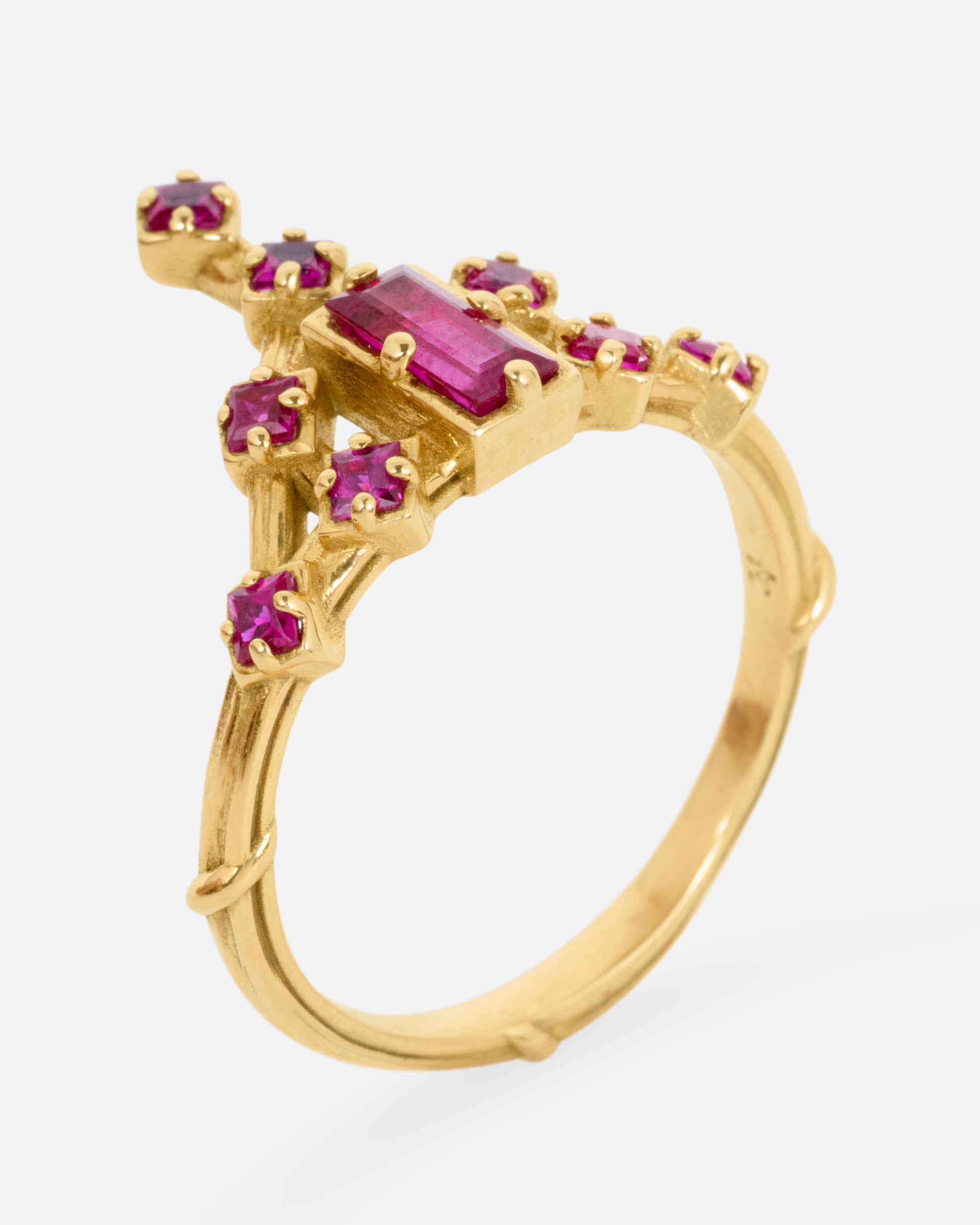 A yellow gold ring with a baguette ruby and princess cut ruby accent. Shown from standing up from the side.